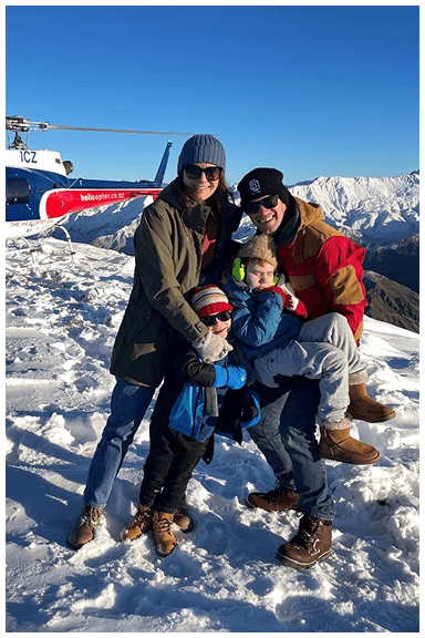 Family on a snowy mountain in New Zealand with a helicopter in the background, father holding his son