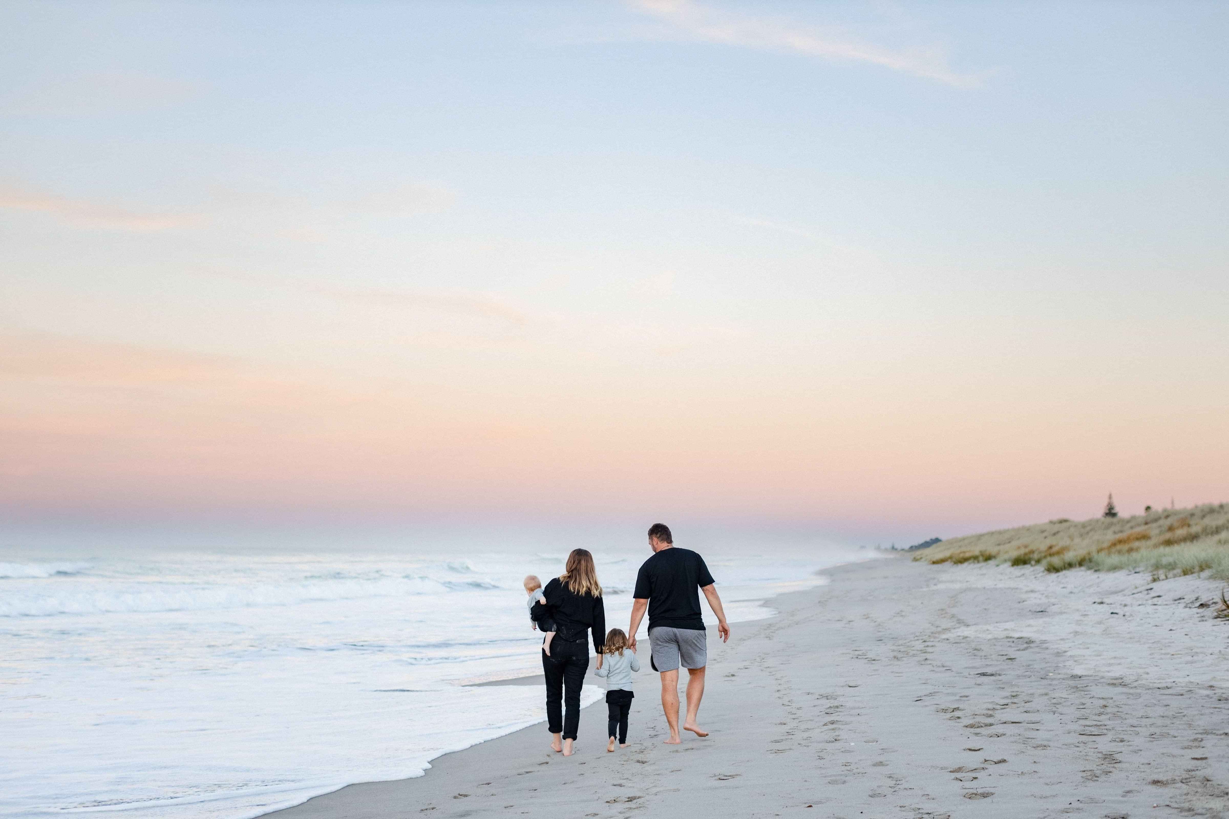 A family of four walking along the beach at sunset.