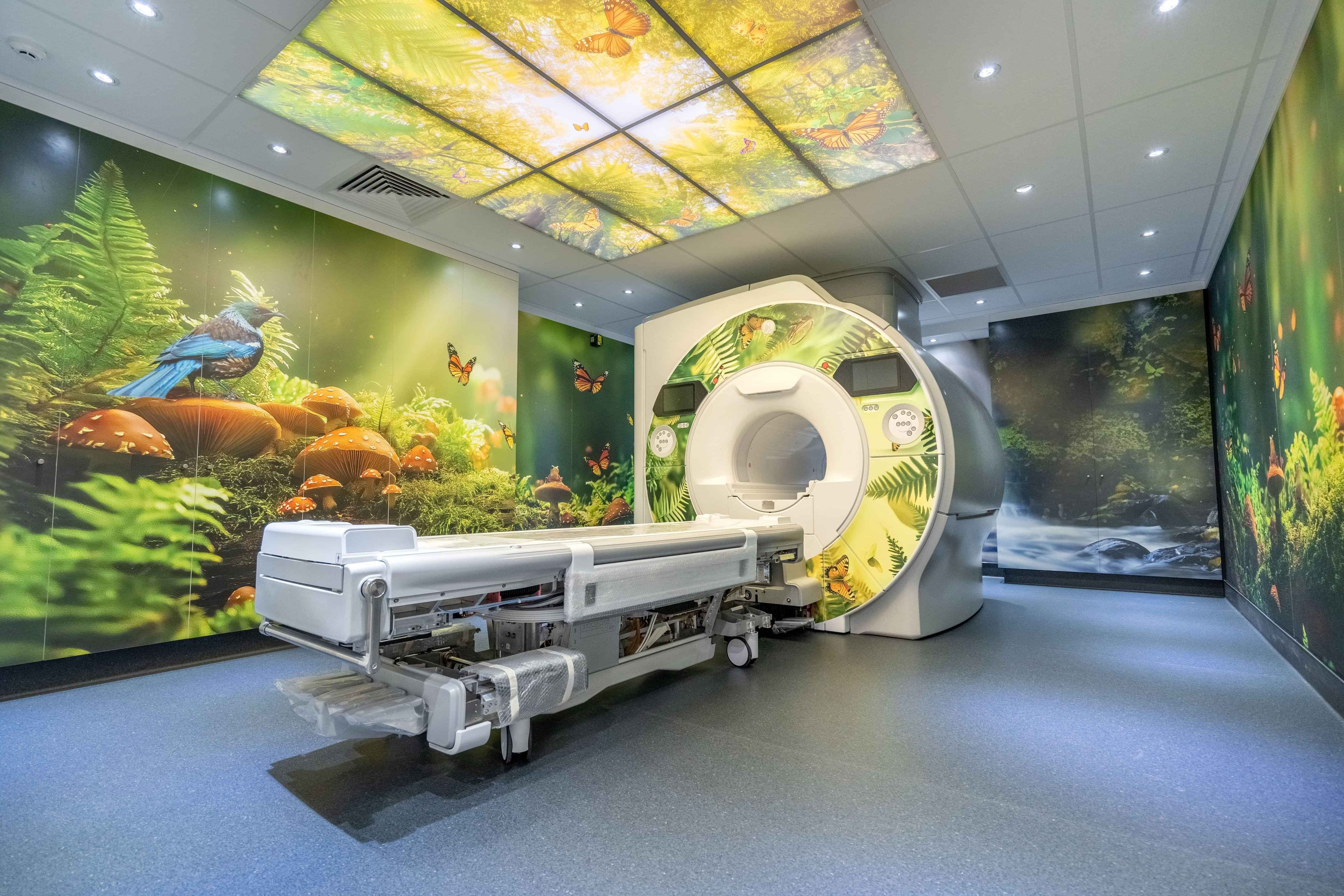 An MRI Machine in a brightly-coloured room decorated with soothing natural forest scenes.