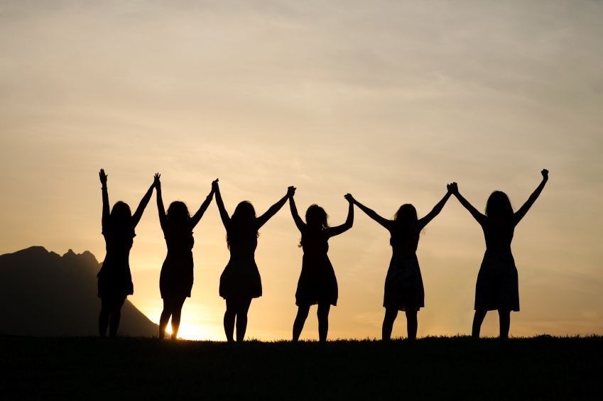 The silhouette of 6 women holding hands with them in the air