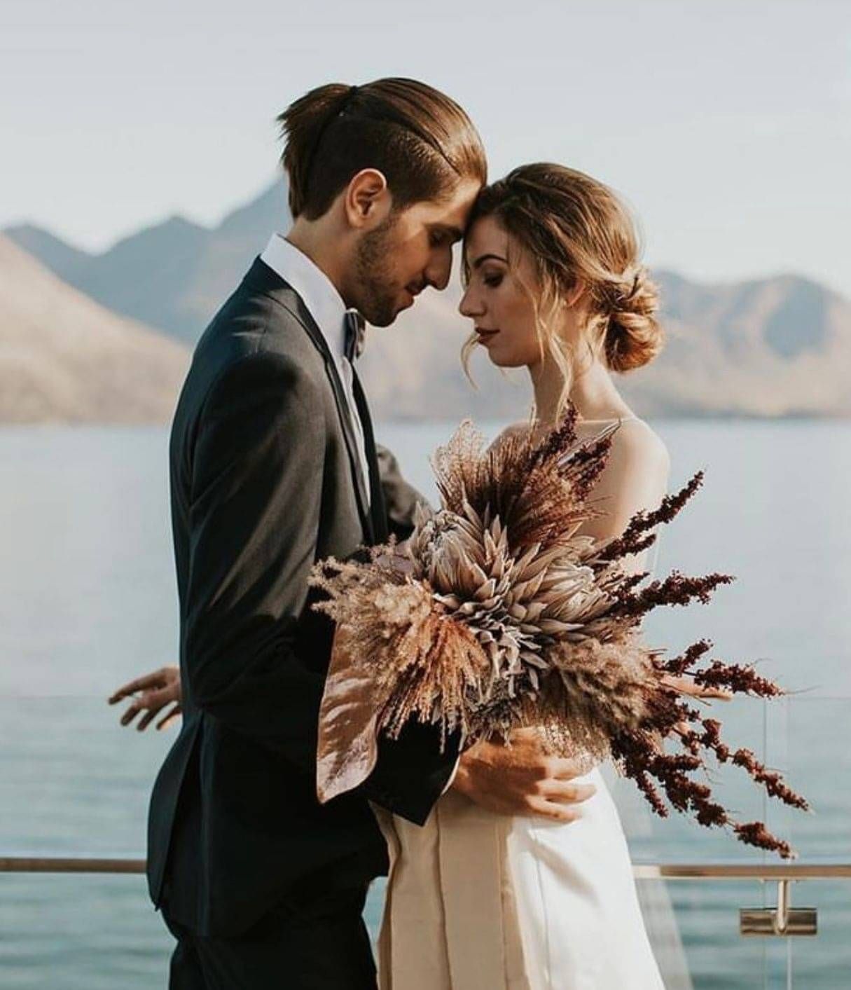 A bride and groom embracing infront of a lake view in Queenstown. Hairstyle by Georgie.