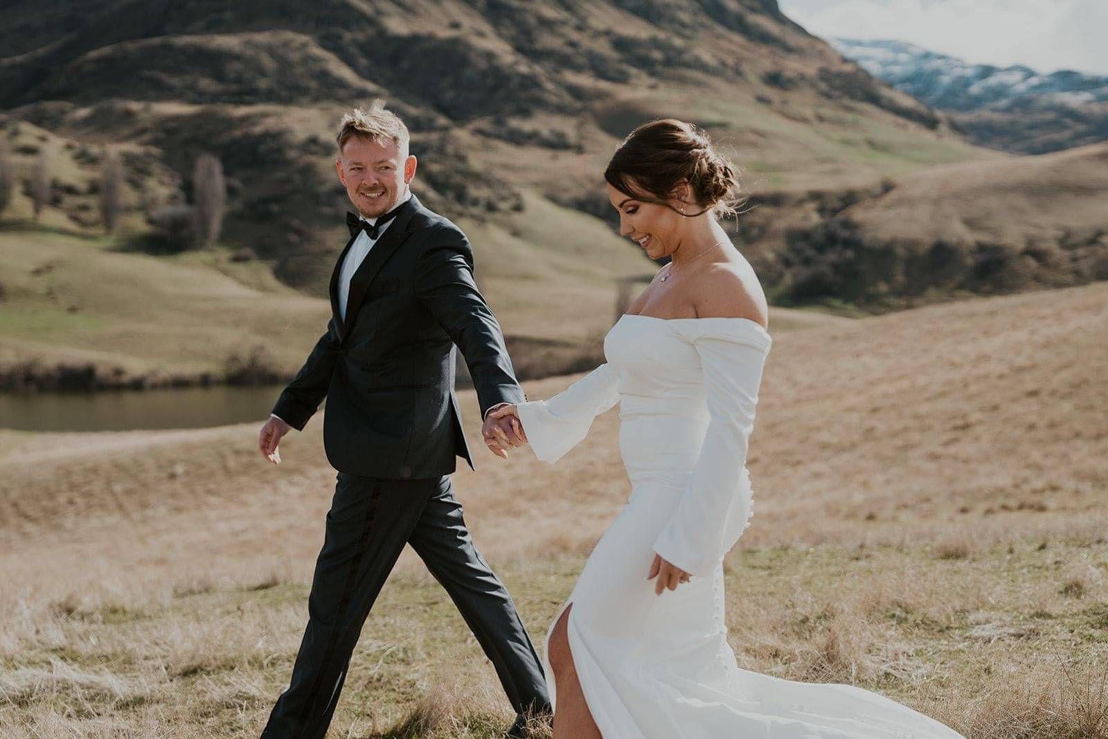 A bride and groom walking together through the mountains in Queenstown. Brides hair up by Georgie.