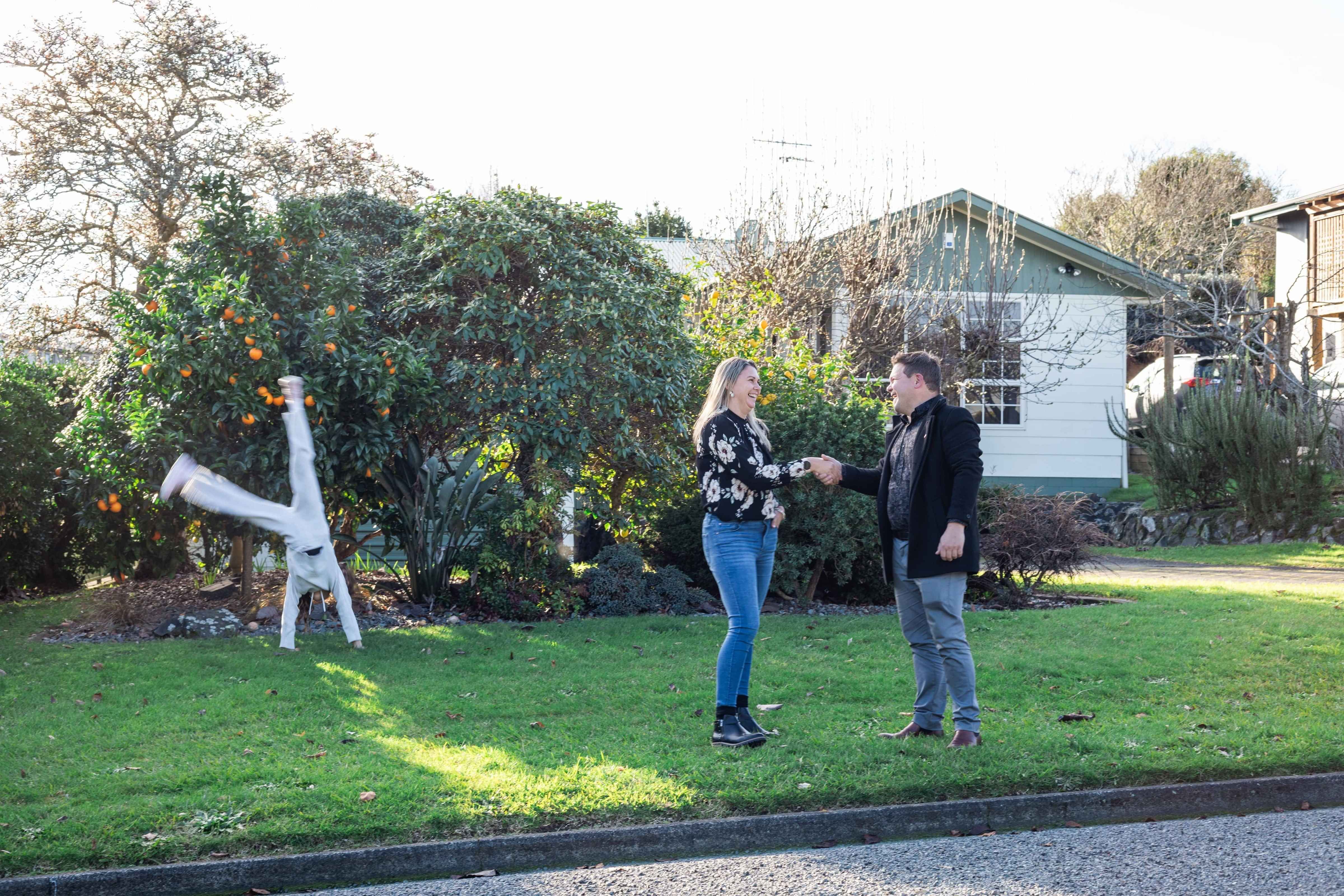 Insurance Adviser shaking hands with a young mother, her child doing cartwheels in the background