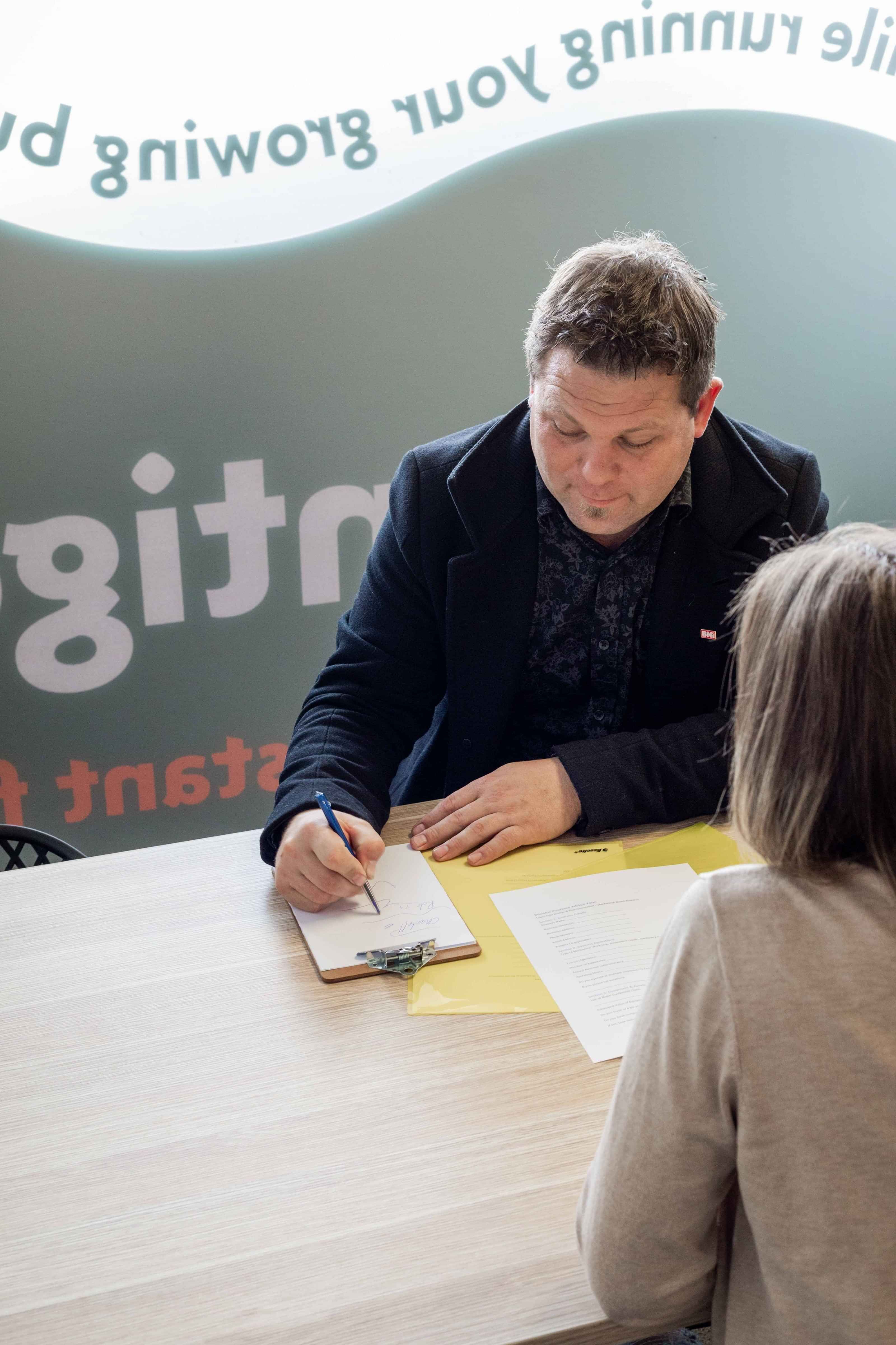 Writing notes in a meeting with a business owner and Insurance Adviser