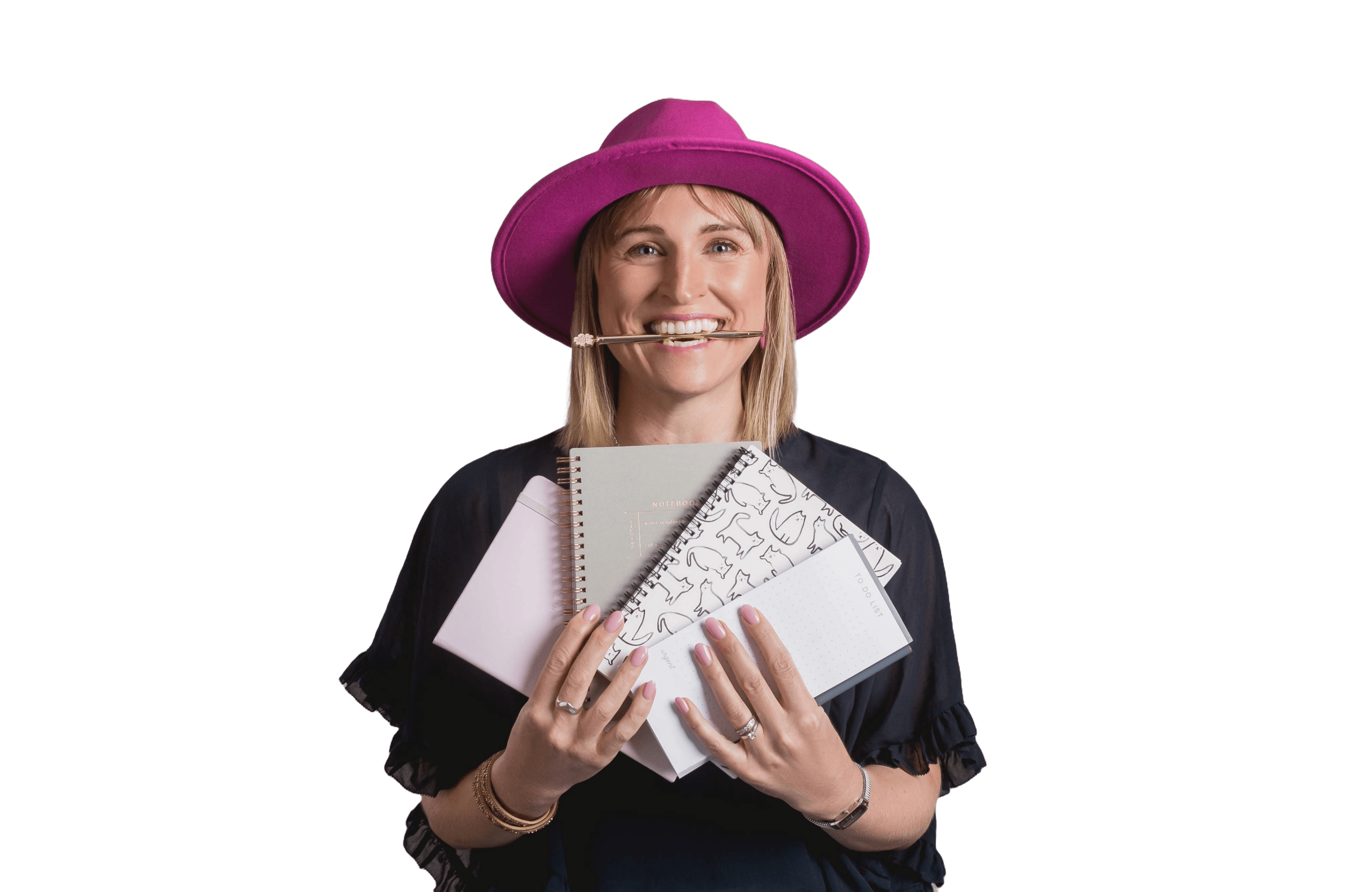 Renee Murphy wearing a pink fedora hat. She's holding a bunch of notebooks and has a smile on her face and a pen in her mouth