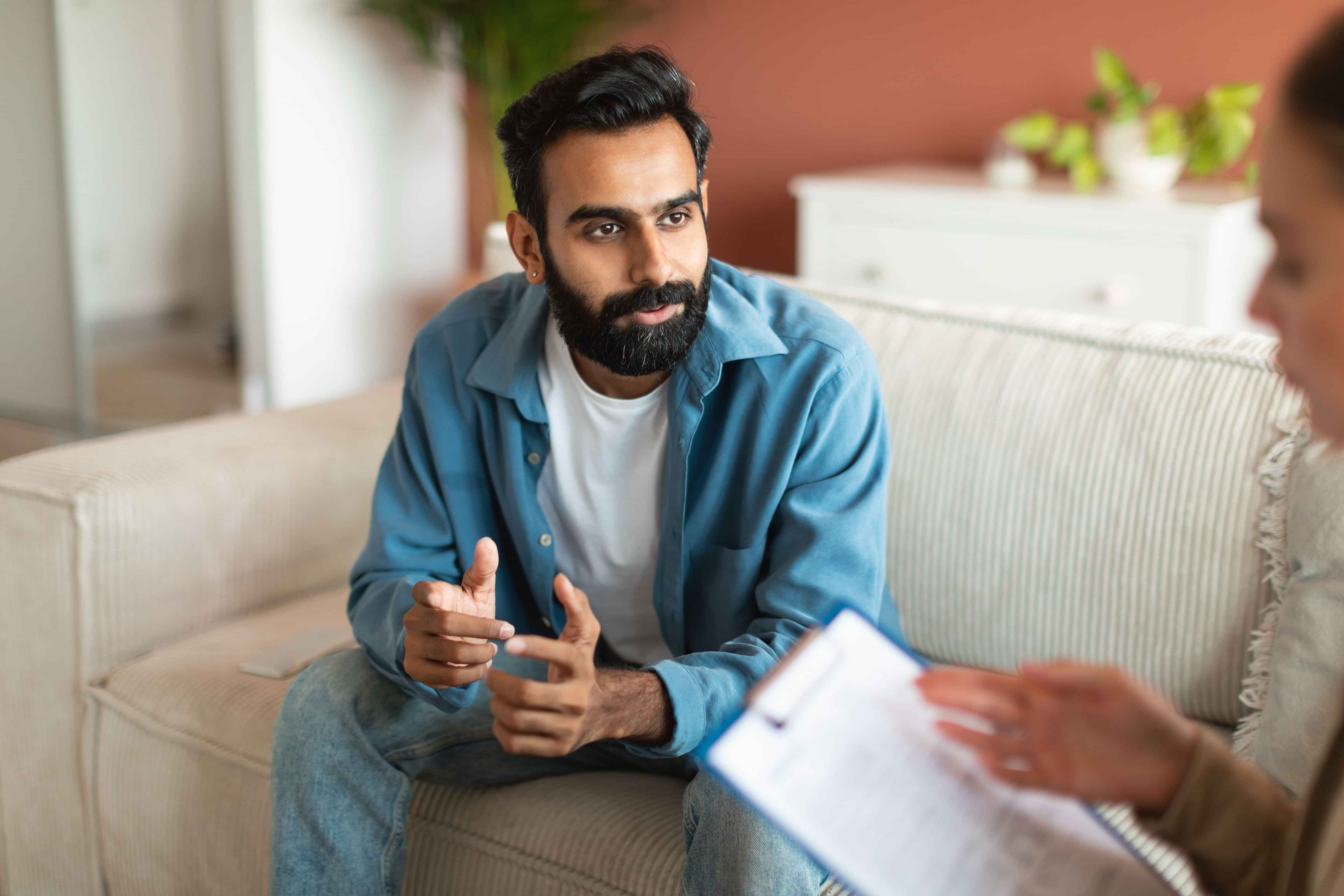 Young Indian man consulting with professional psychologist sitting indoors