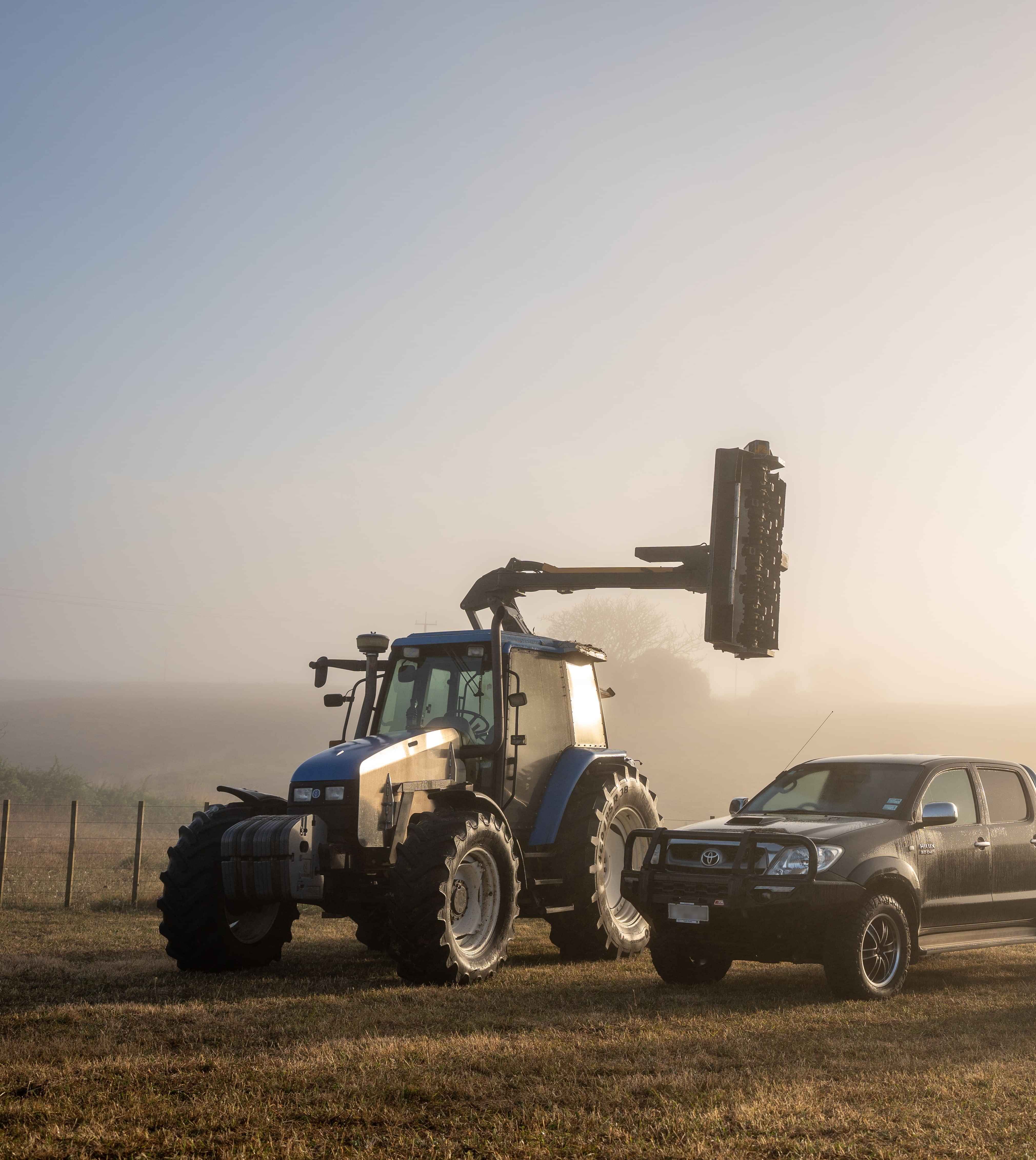 Image of a blue Holland tractor set up for hedge cutting and Toyota ute on a lifestyle block. Habraken Fencing, Waikato.