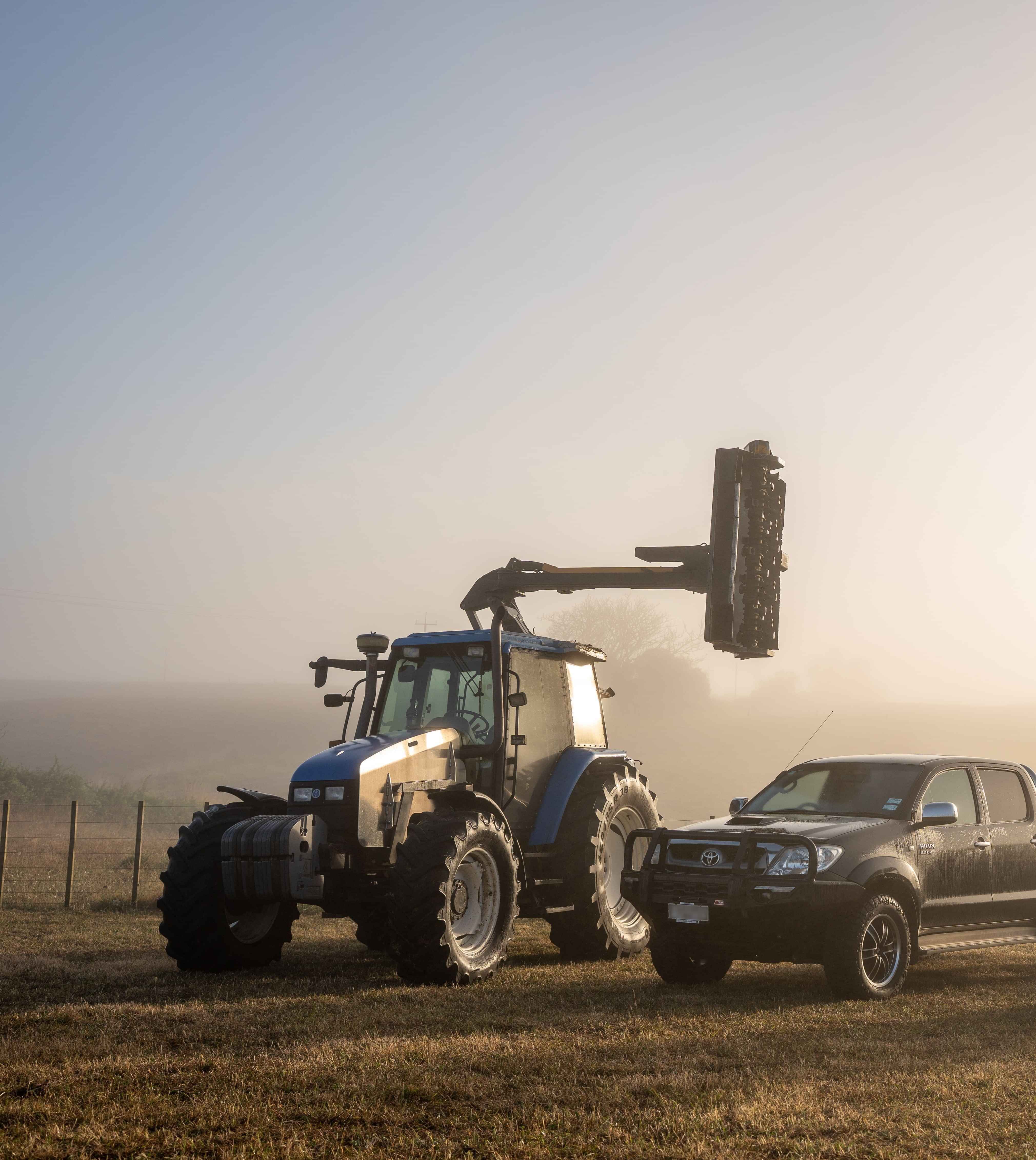 Image of a blue Holland tractor set up for hedge cutting and Toyota ute on a lifestyle block. Habraken Fencing, Waikato.