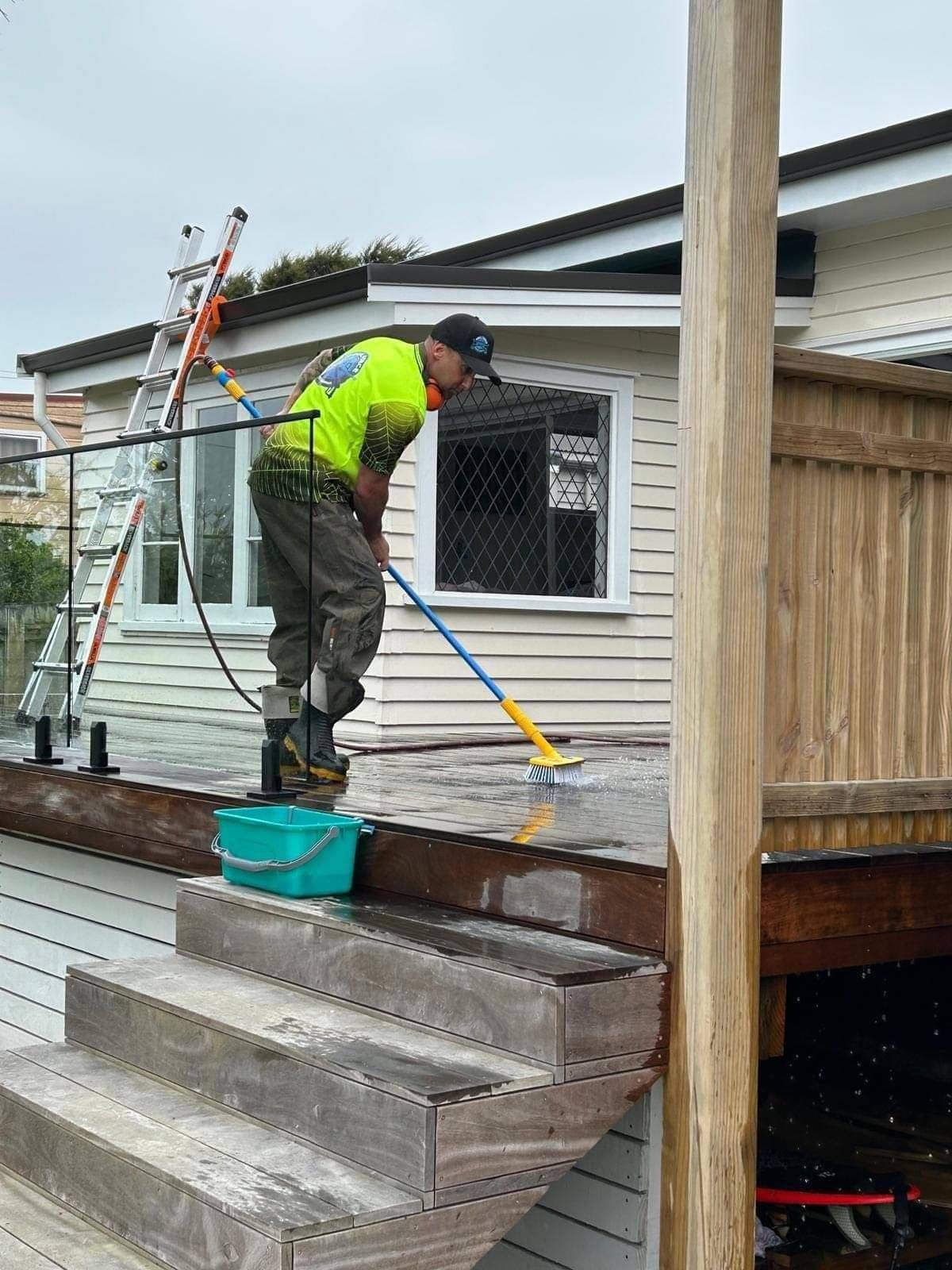 Photo of Aqua Force team member scrubbing and cleaning a wooden timber deck at a Hamilton home
