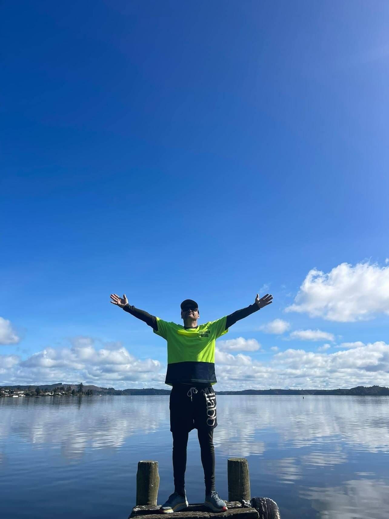 Sam standing arms wide open 'free' infront of a alke with mountain backdrop