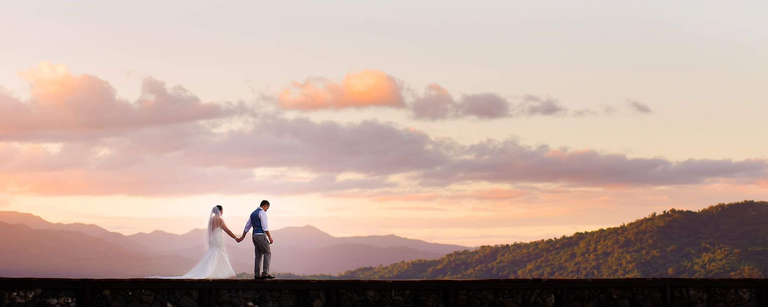 Couple standing together at sunset overlooking the ocean, symbolising a destination wedding or romantic escape