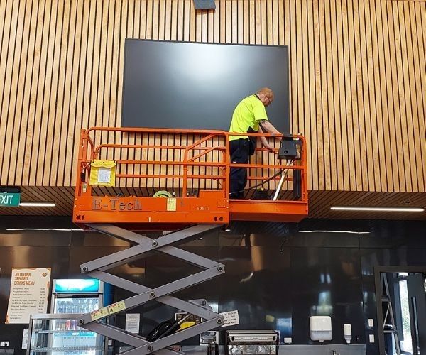 Man in high vis on scissor lift installing large screen
