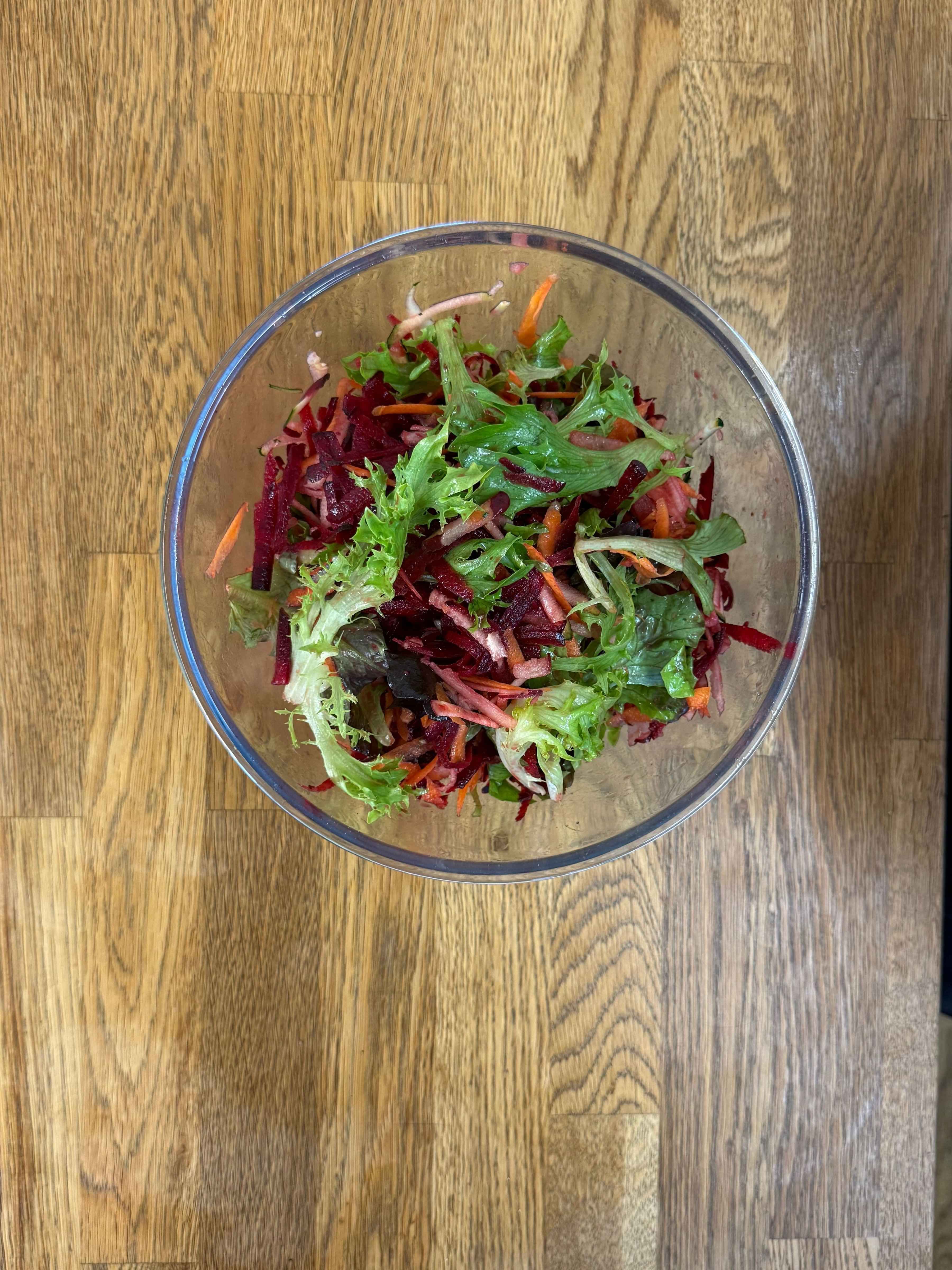 grated salad with lettuce, beetroot, carrot, and dressing in a glass bowl