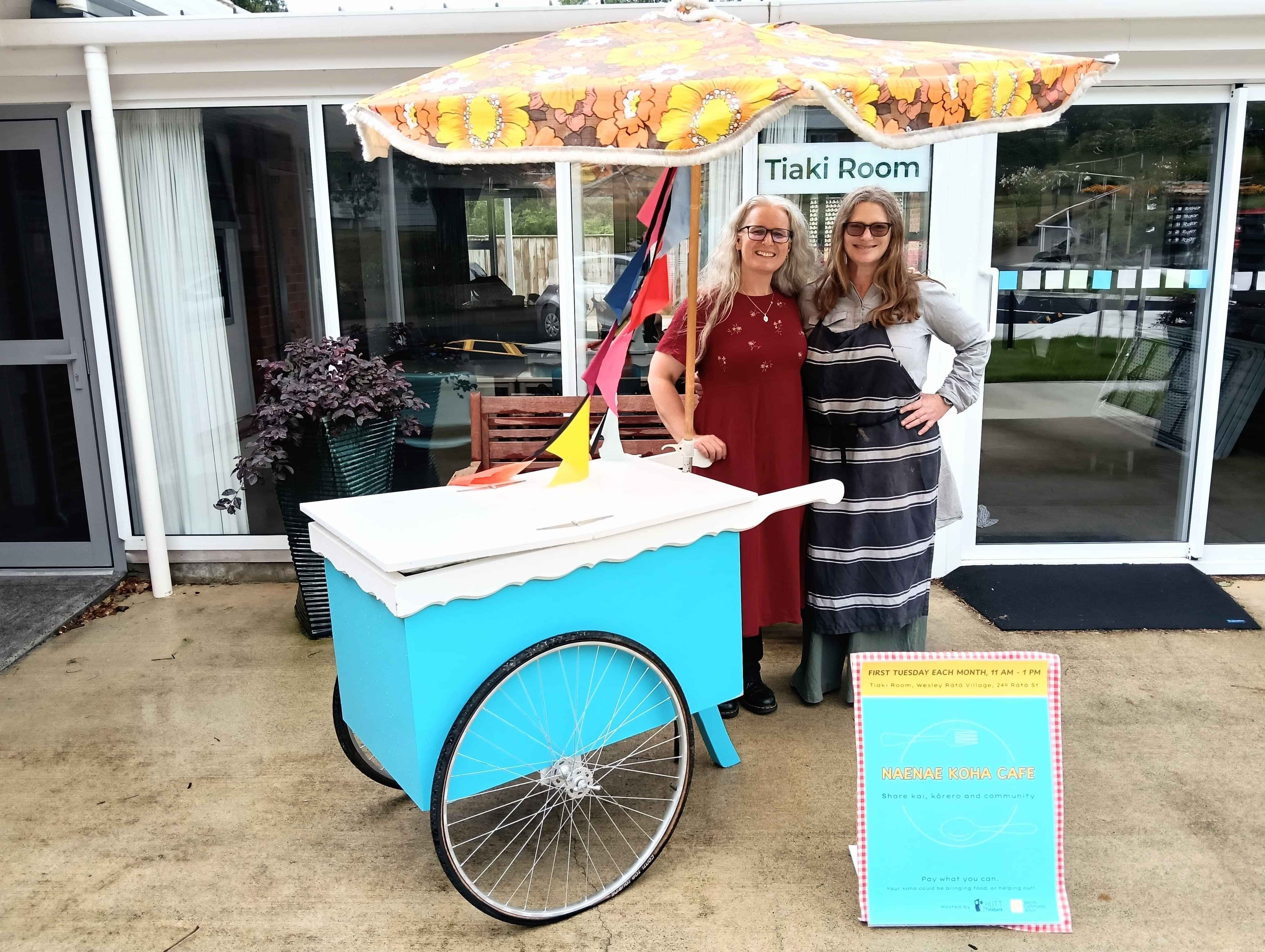 People in front of Naenae Koha Cafe space , with bunting, cute handcart, vintage sun umbrella.