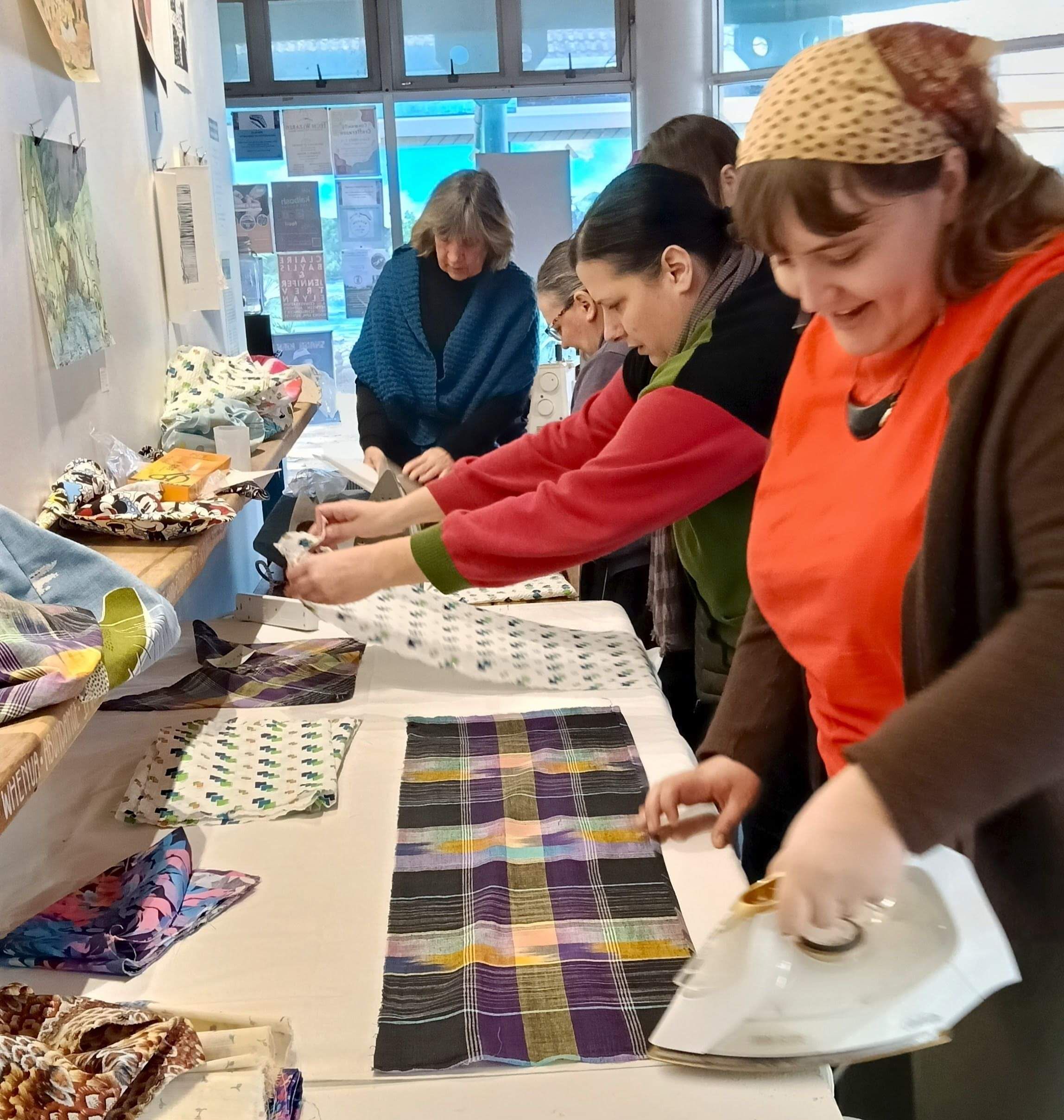 A group of people cutting up squares of scrap fabric and ironing them for sewing, laughing and concentrating.