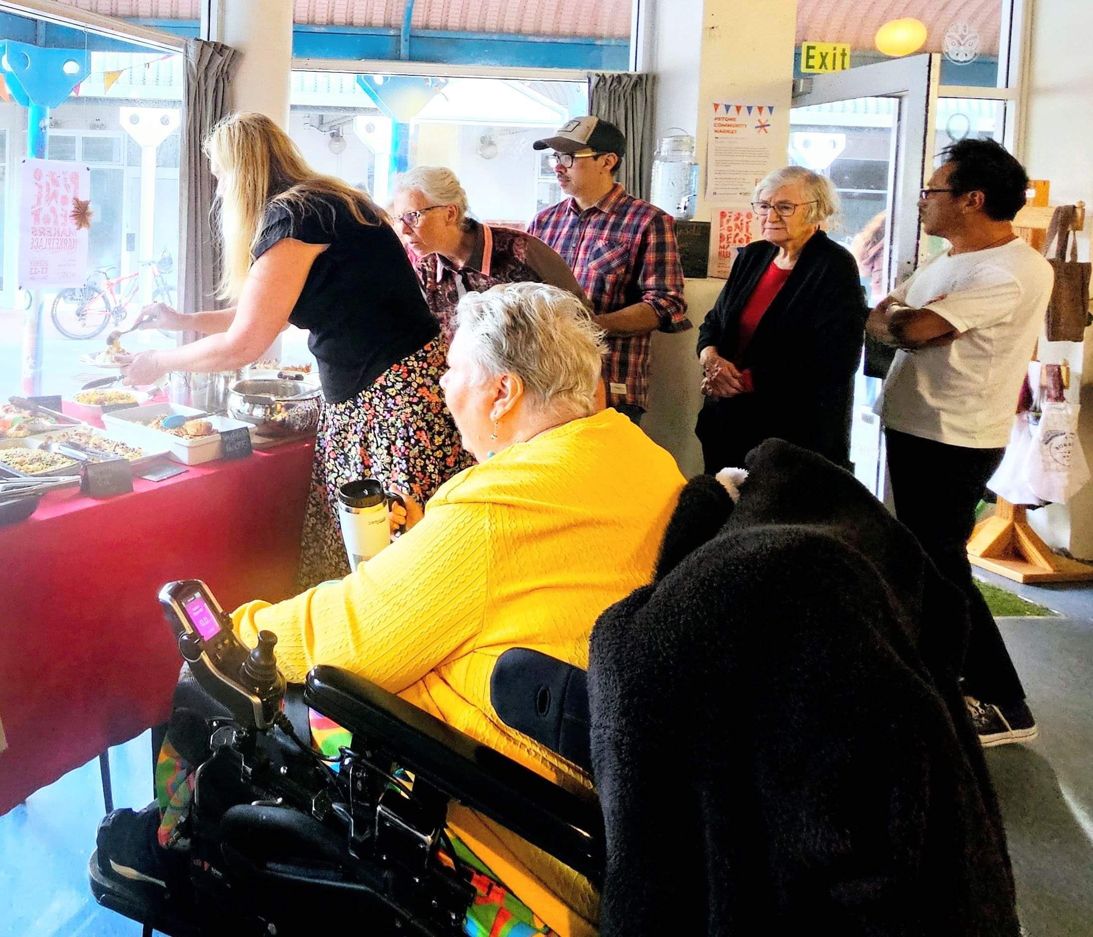 People serving themselves at a potluck, with a wheelchair uszer in the foregound