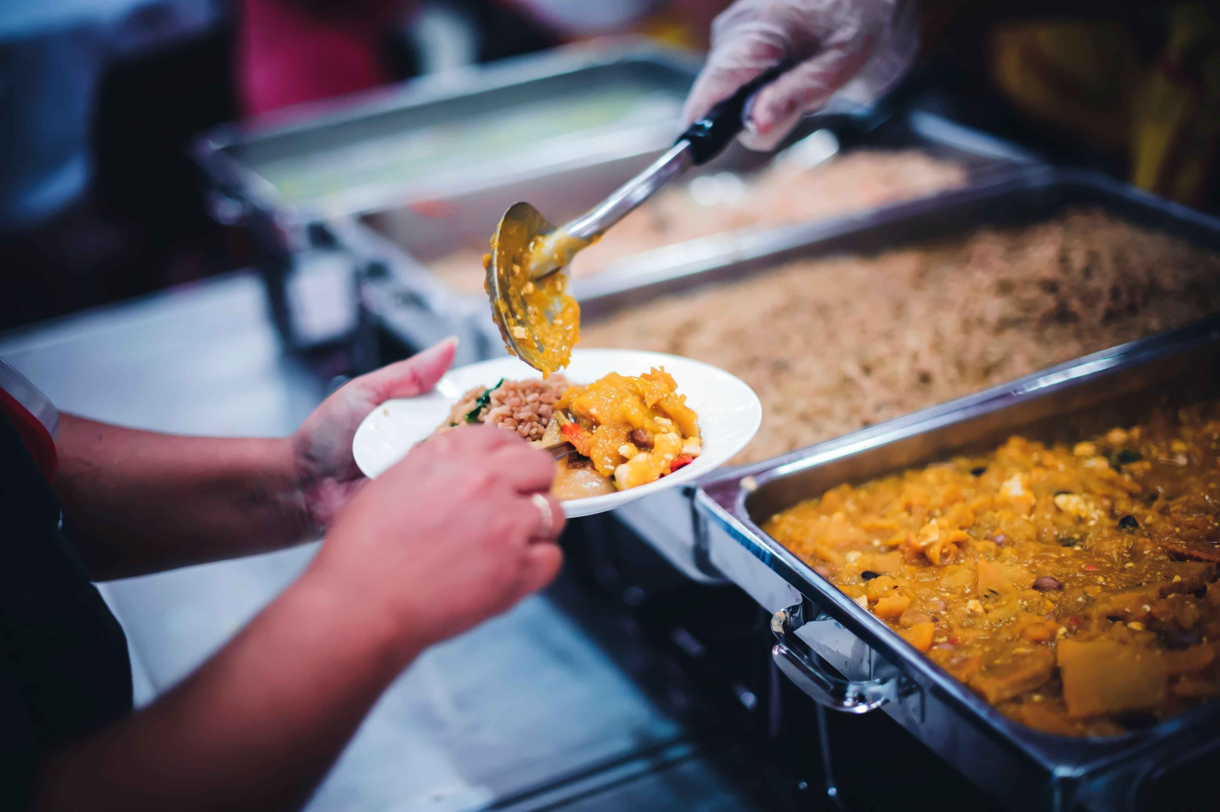 Someone's hands holding a plate while food from a warmer gets served onto it.