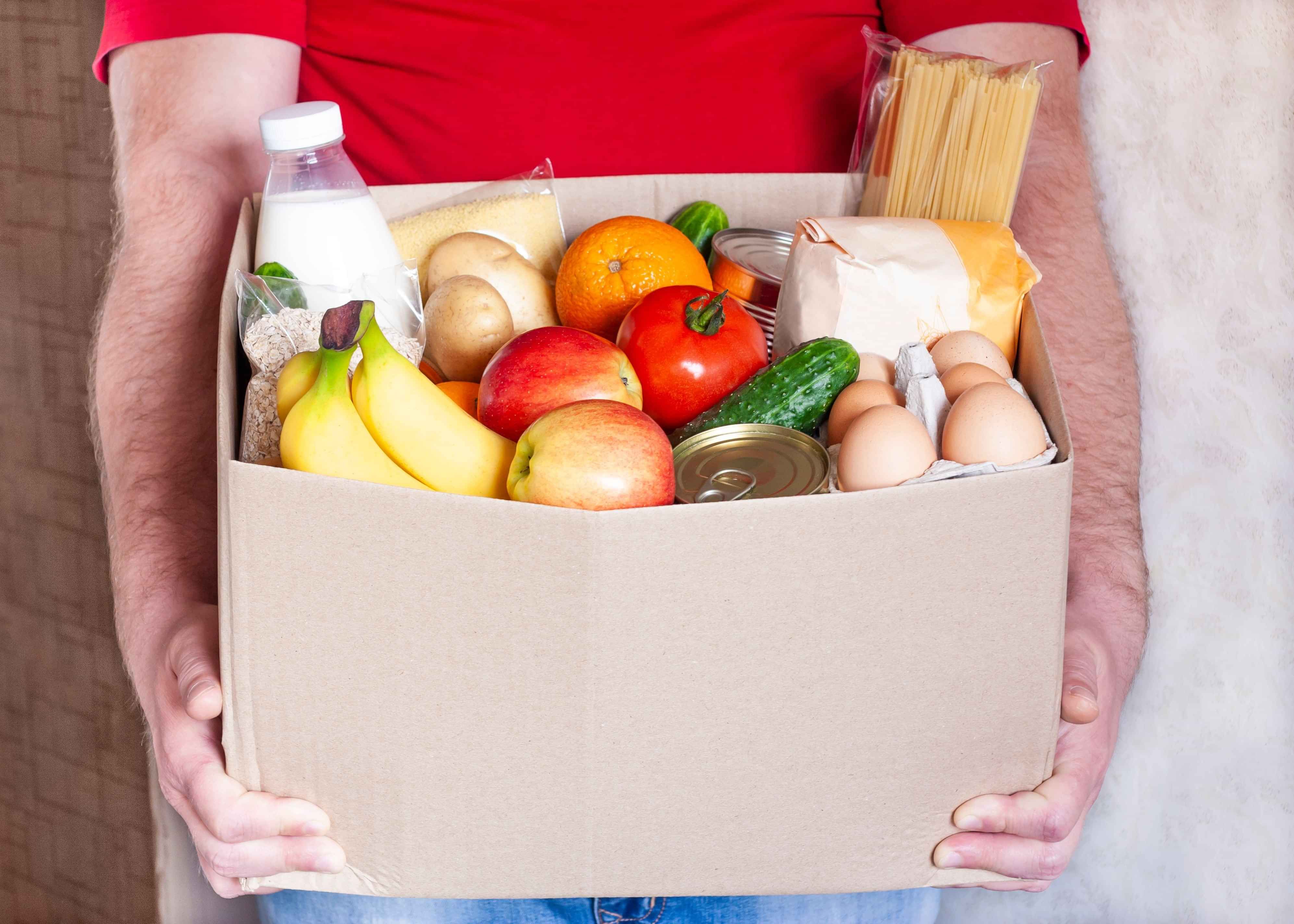 A cardboard box of groceries - fresh fruit, veges, eggs and milk.