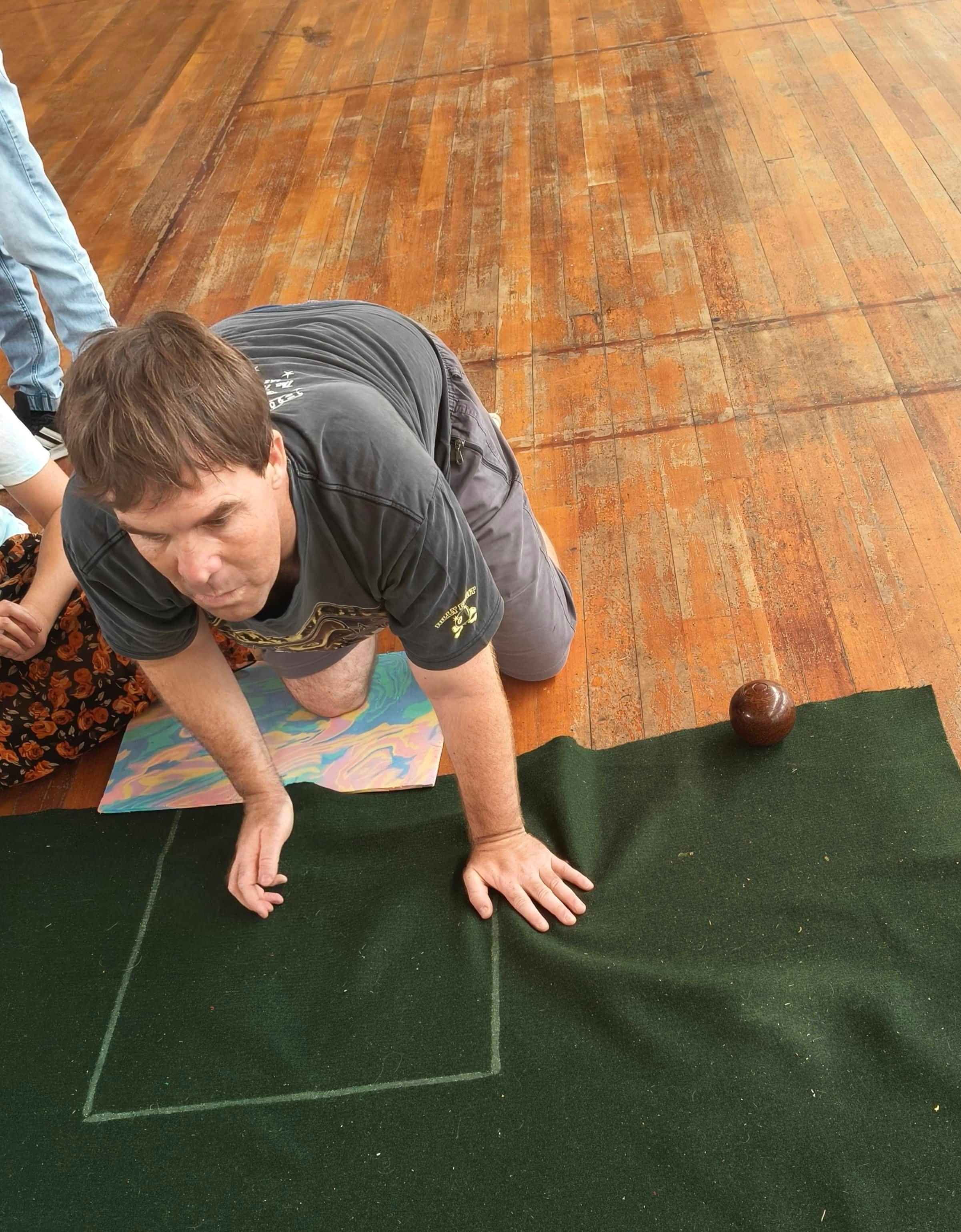 A young man on his hands and knees playing indoor bowls.