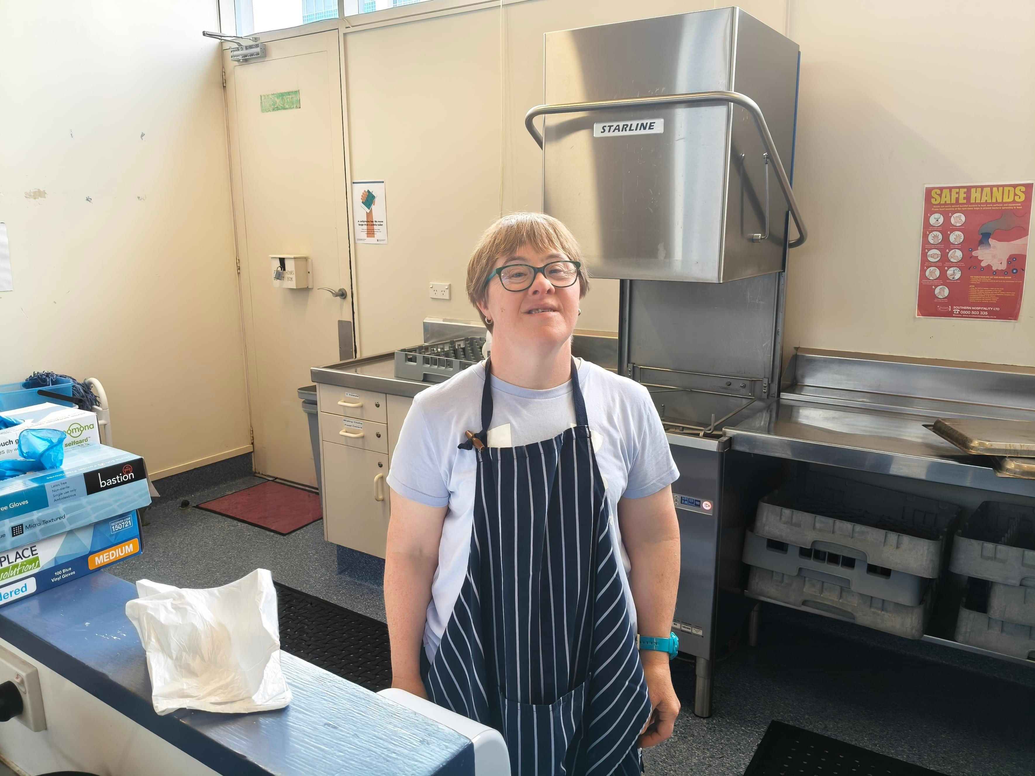A young adult wearing an apron in the kitchen.