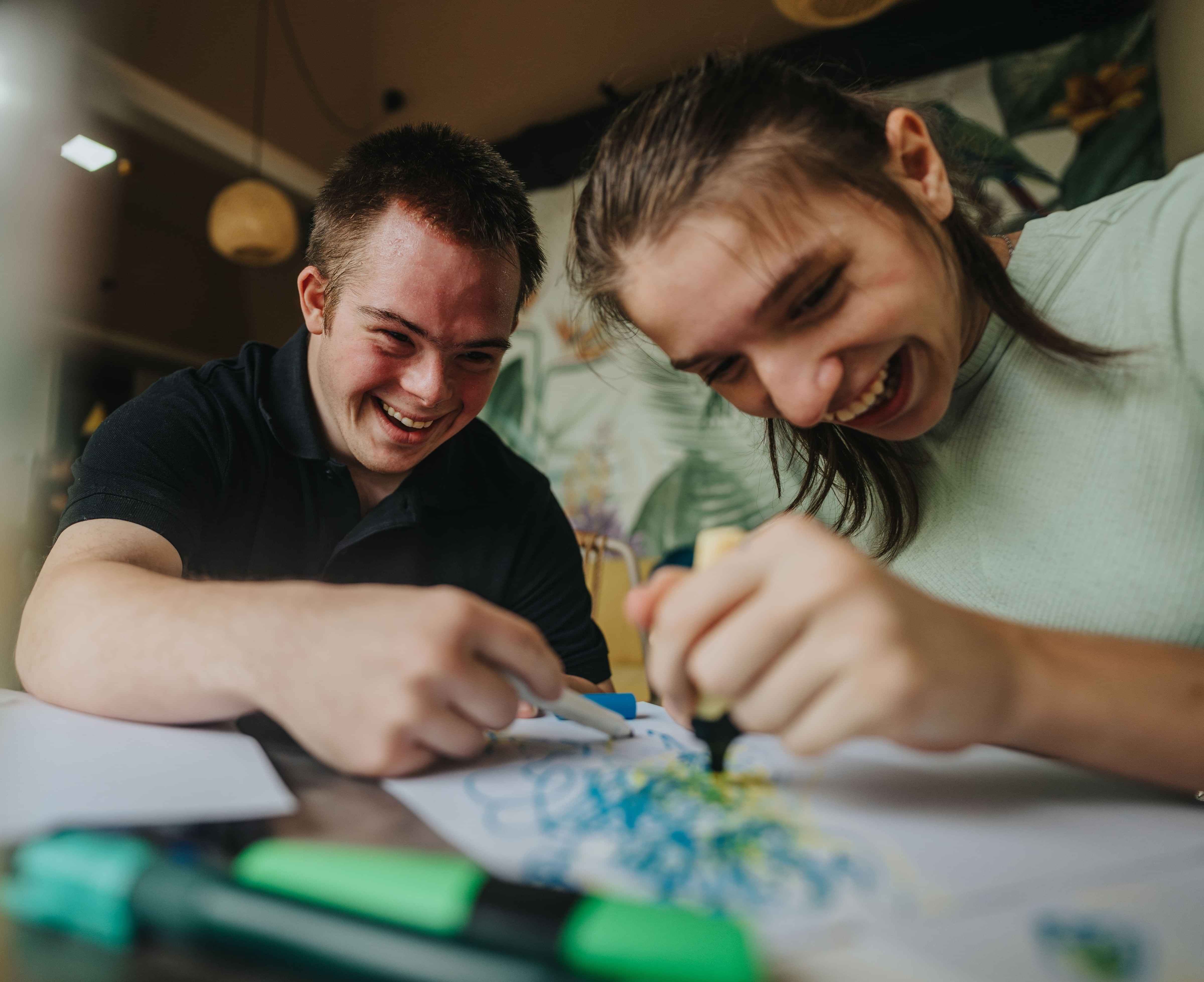 Two young men laughing and working on a joint art project with coloured pens.