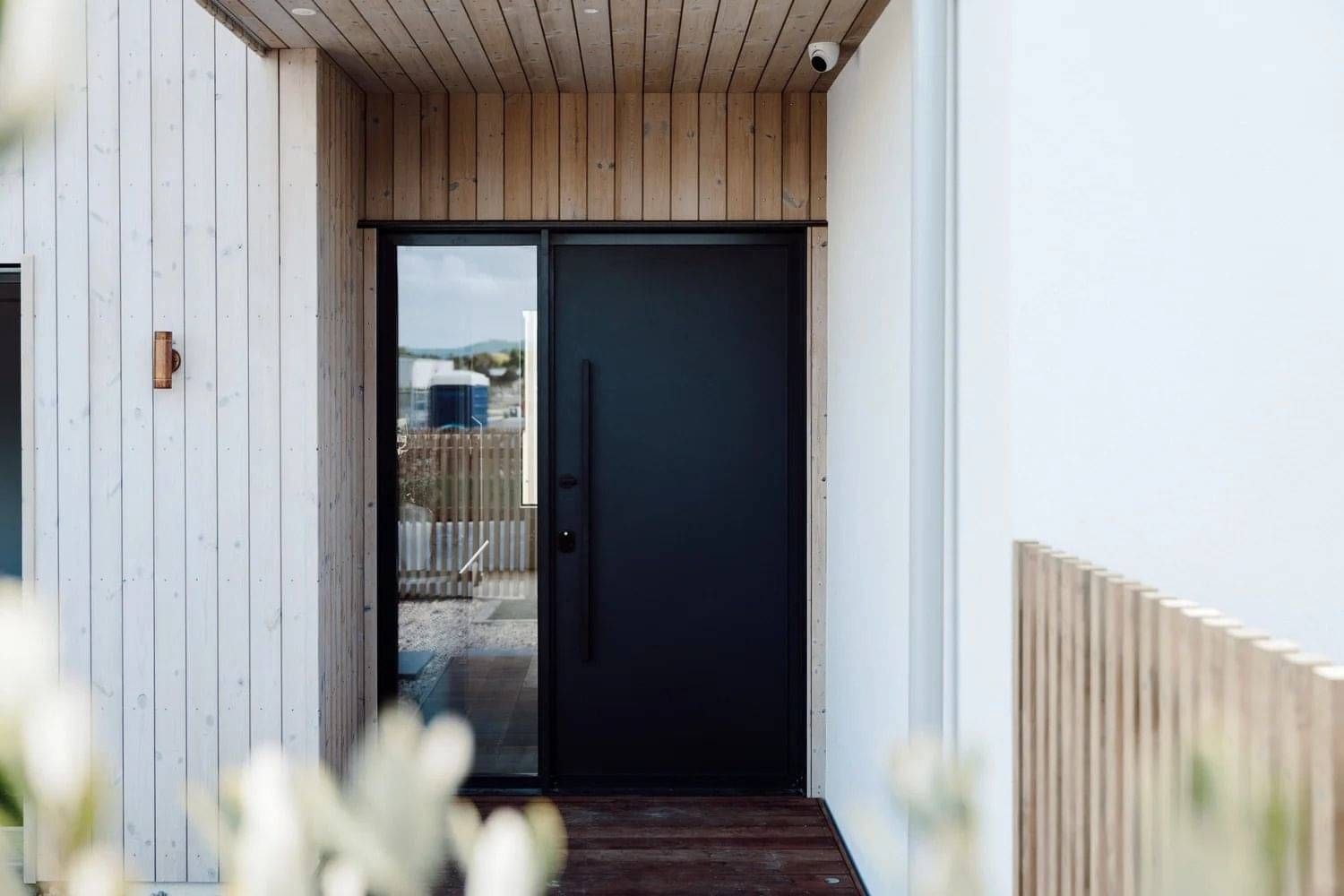Black front door with black hardware against a white washed vertical wooden paneling