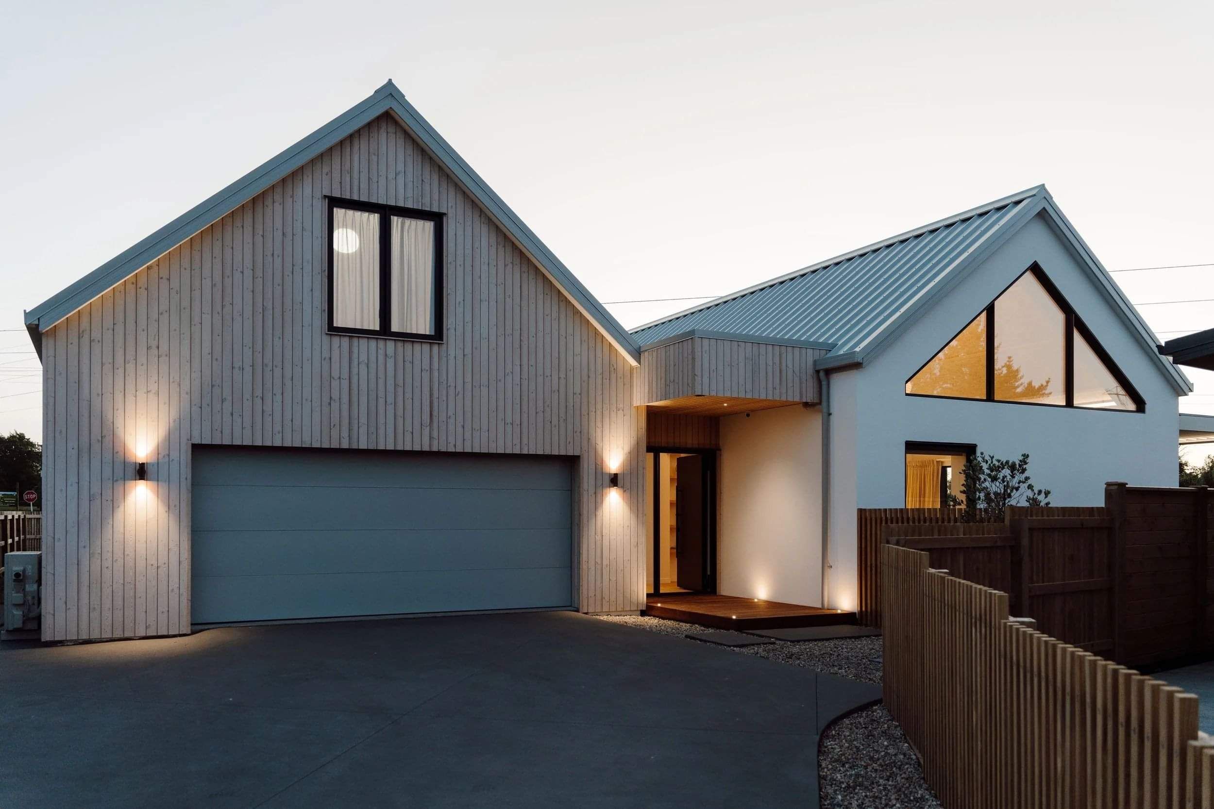 Exterior vertical wooden paneling on a home at dusk with lights on inside