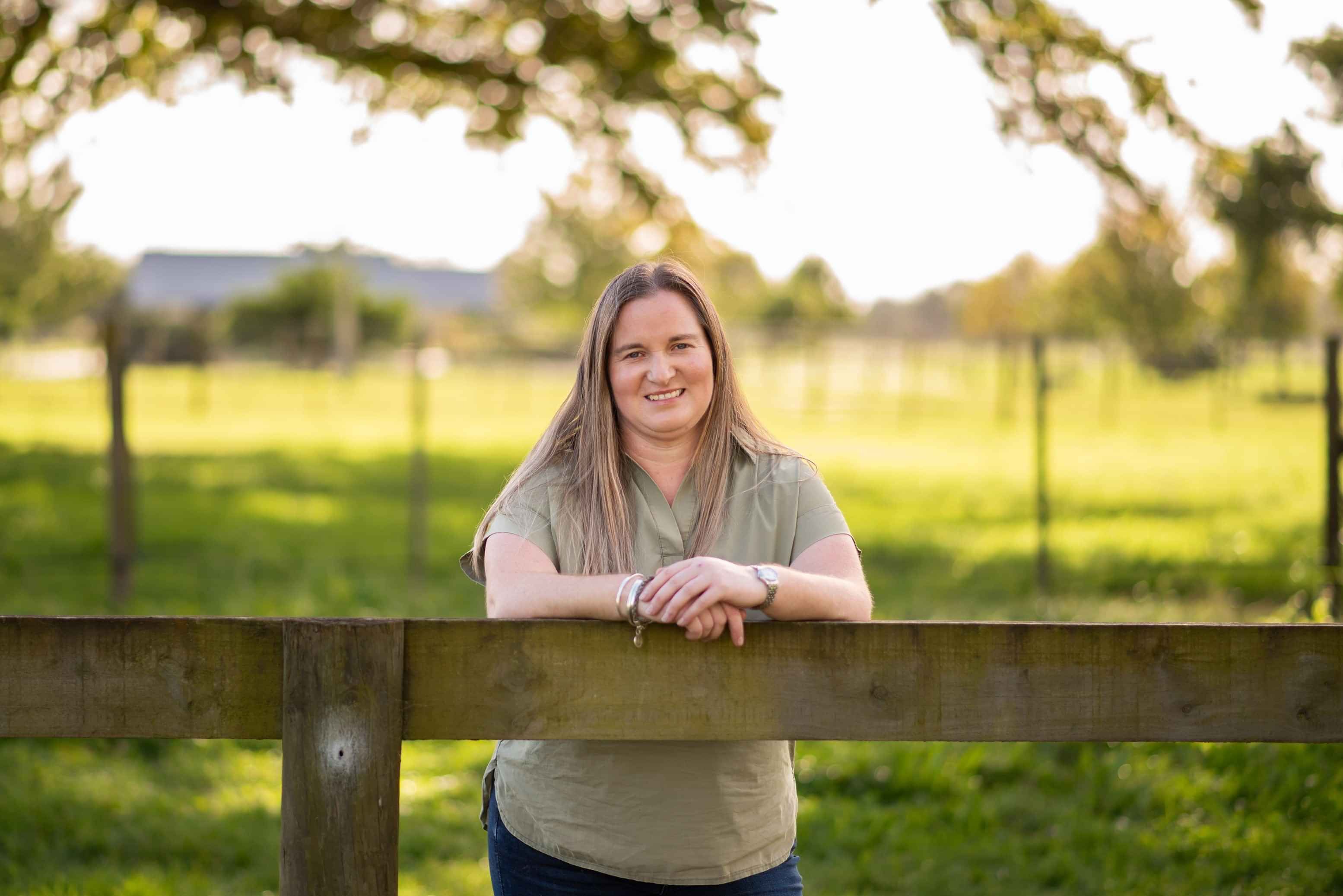 Merryn Telfer, smiling while leaning on her farm fence