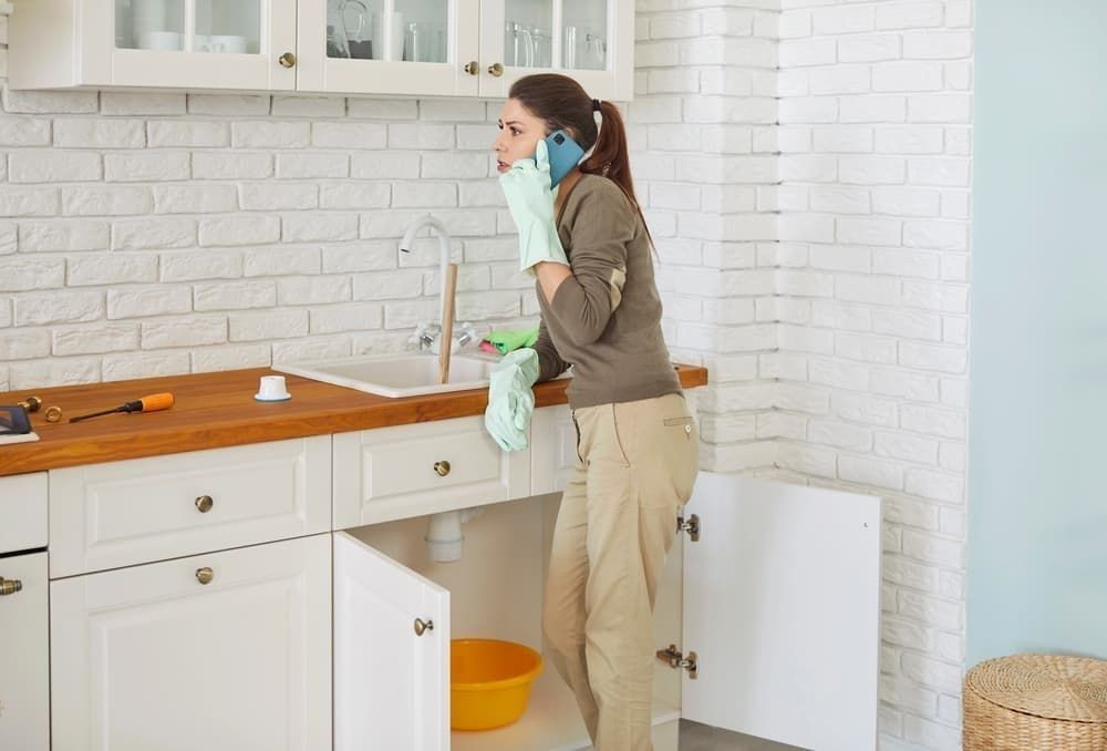 Young woman talking by mobile phone advising how to unclog a sink drain with plumber