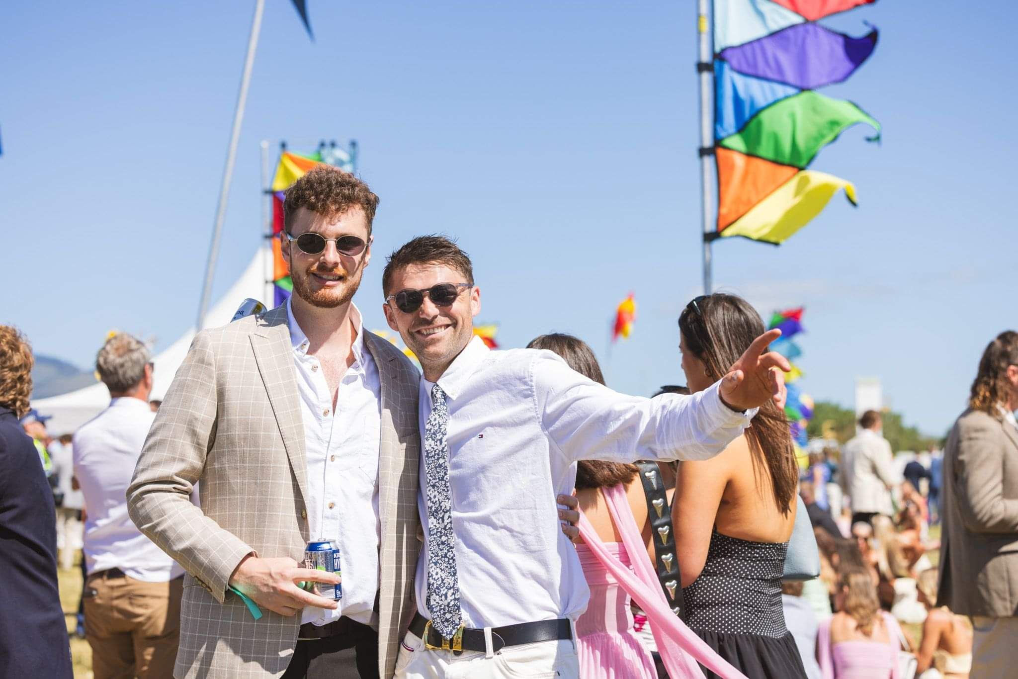 Two guys dressed formally for the race day with sunglasses smiling