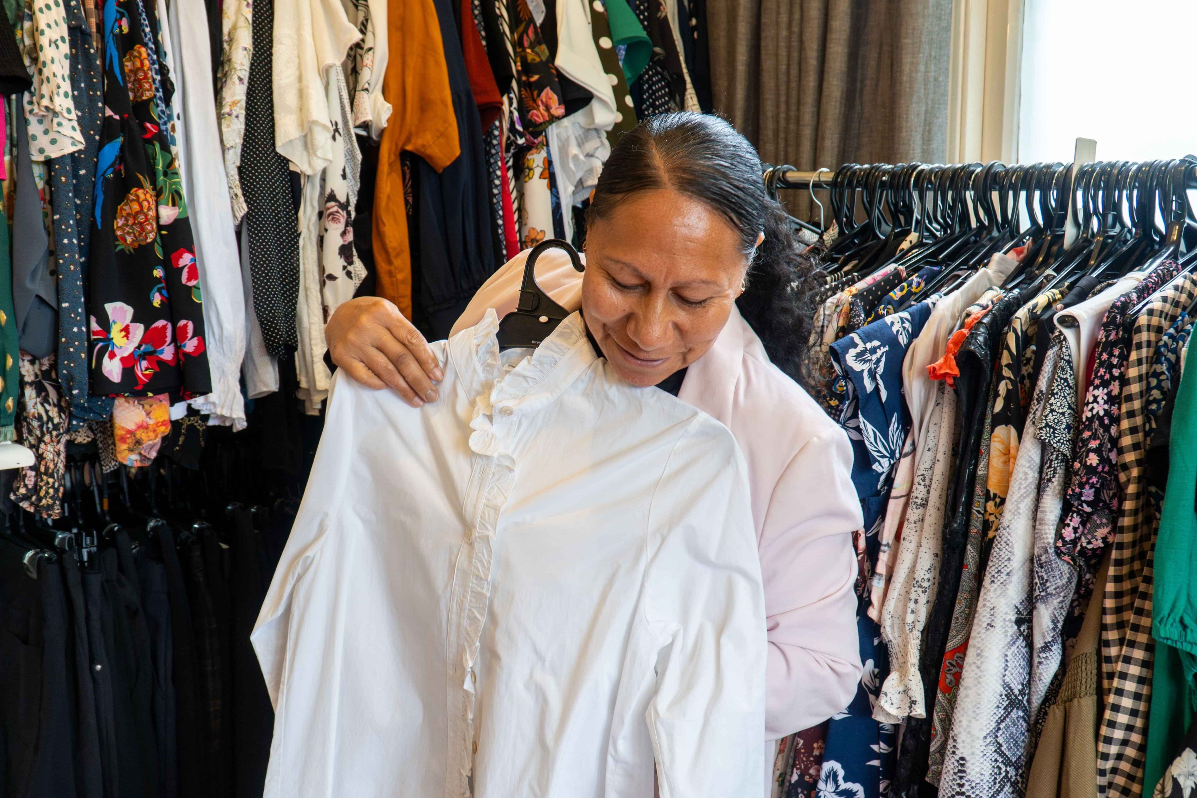 Dress for Success women client smiling down at a white shirt she has chosen in a clothes styling room