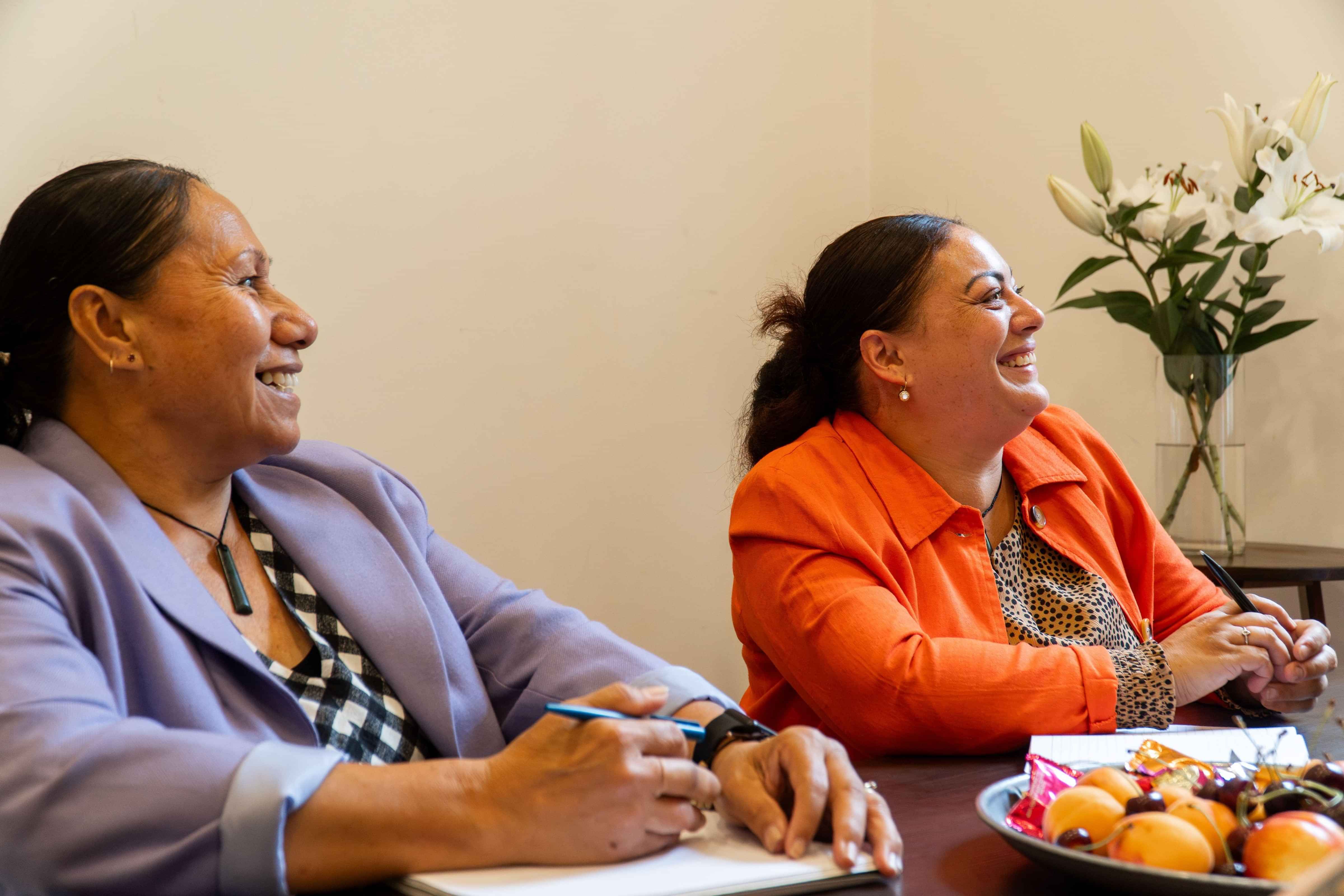 Two Dress for Success clients sit around a table in their careers appointment, smiling about what they are learning.