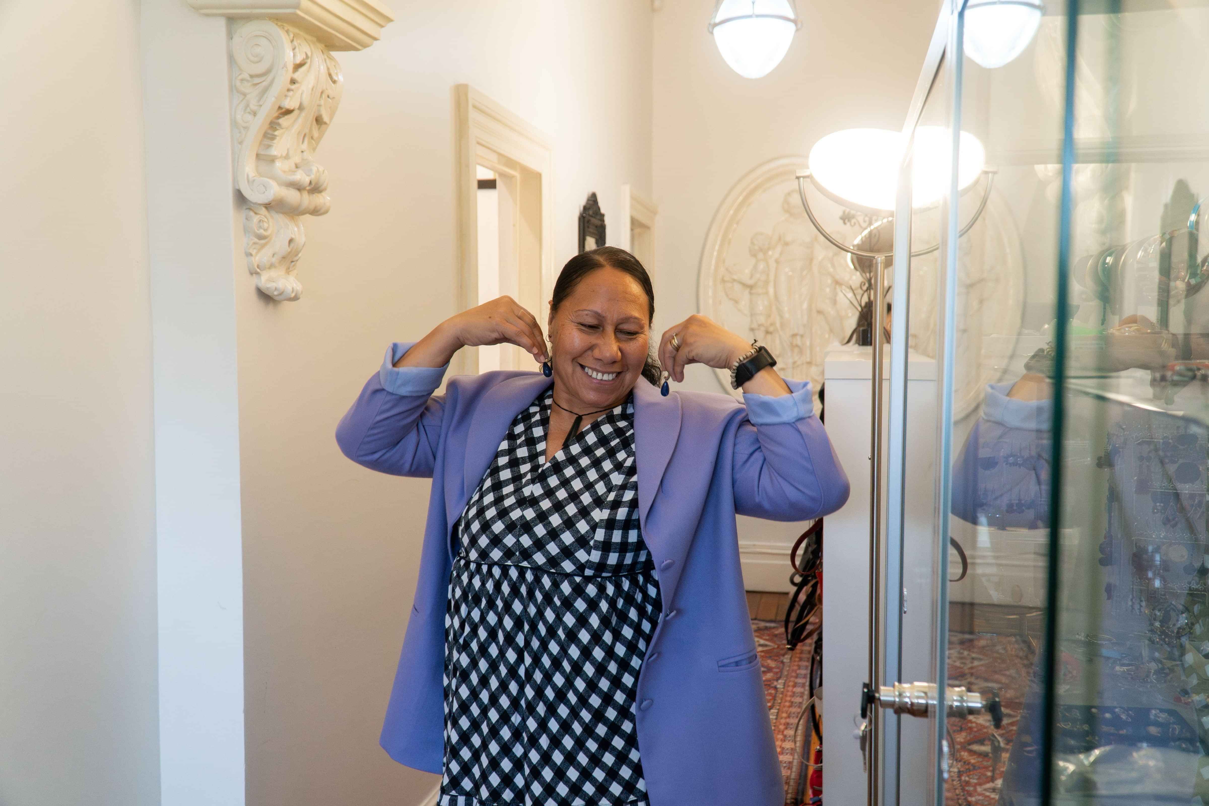 Dress for Success smiles joyfully as she walks up hallway, playfully holds different accessories as if she was trying them on