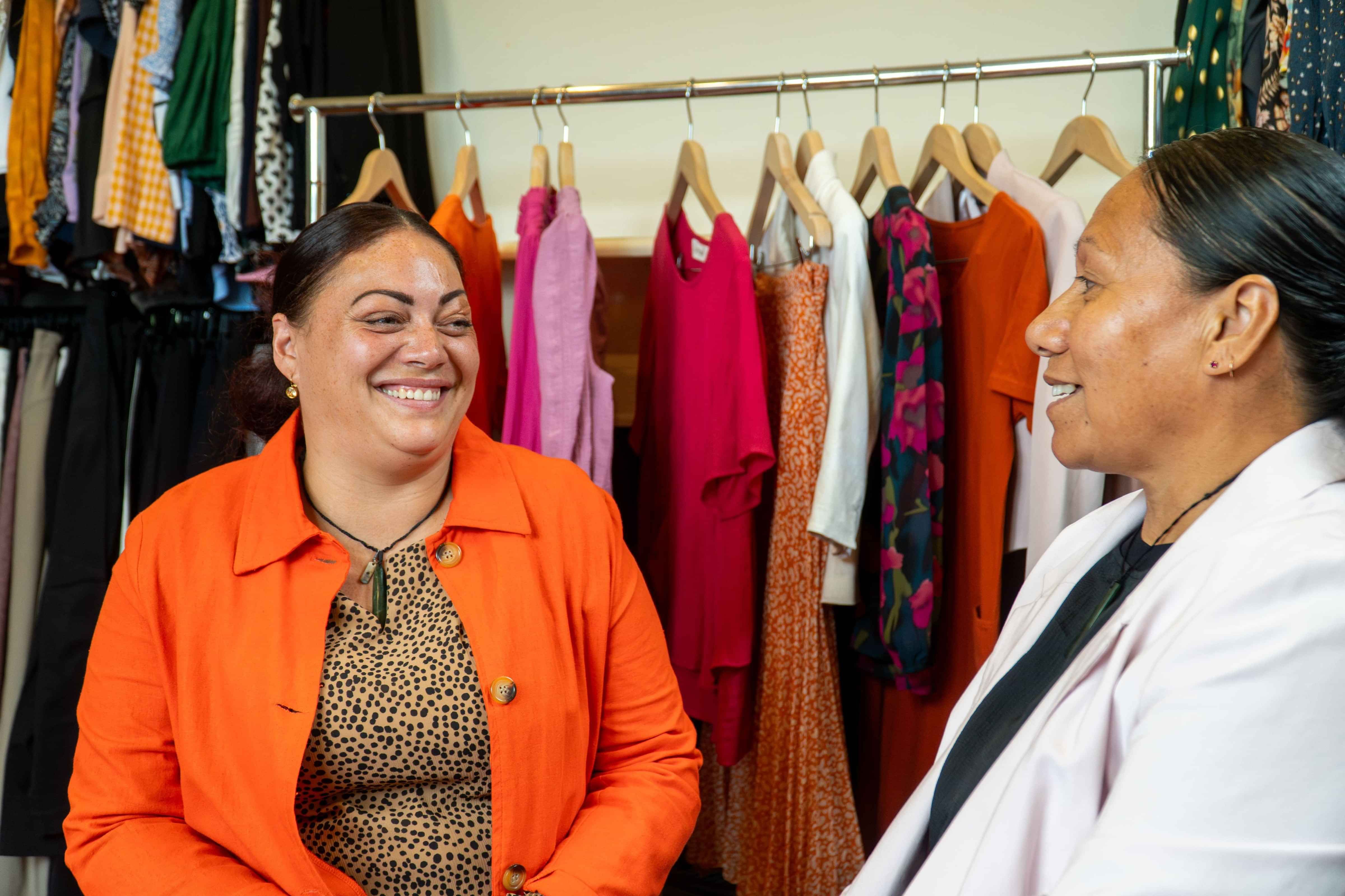 Dress for Success client smiling in a clothes styling room wearing a bright orange jacket