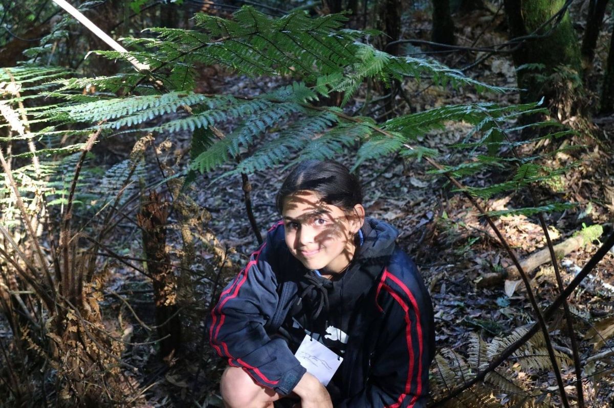 A student sitting under a tree fern with the frond shadow across her face