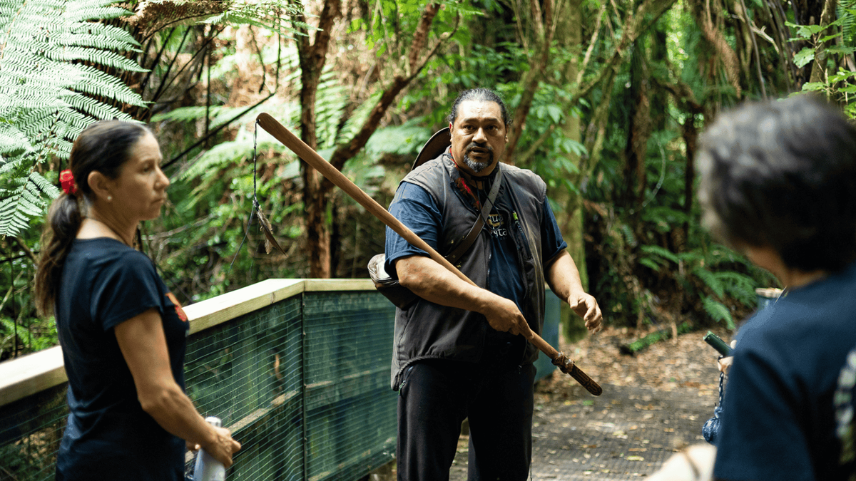 Mana whenua guide holding a taiaha while talking to visitors on the track