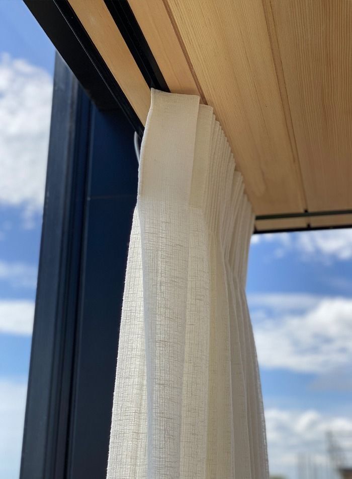 Cream drapery curtain hanging in timber-framed window with blue sky view, commercial curtains by Quality Curtains