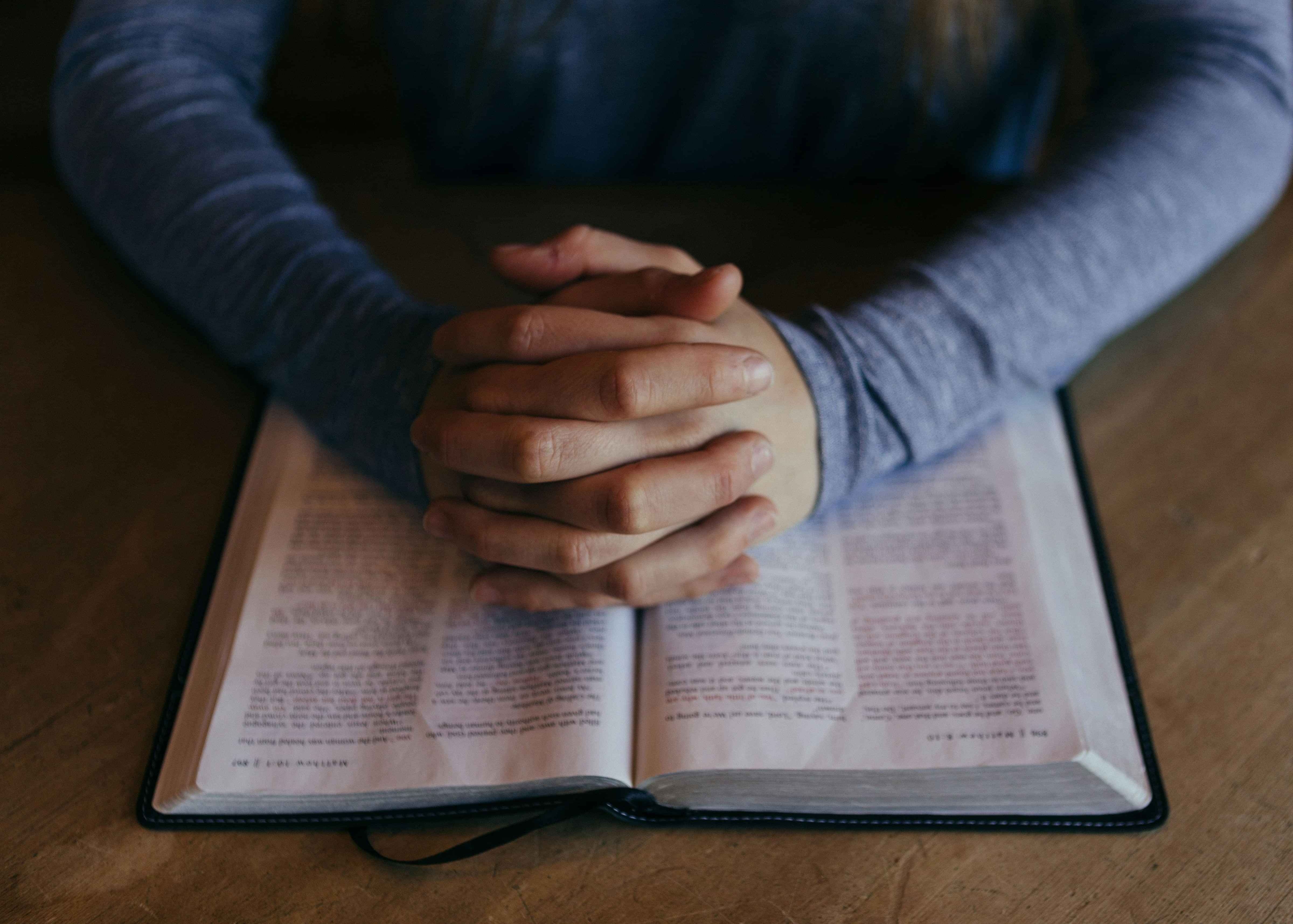 Image of hands clasped in prayer in front of Christian Bible