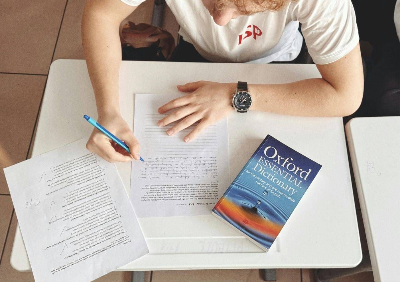 Person studying with an English dictionary and notebook, preparing for the AEWV English language requirement