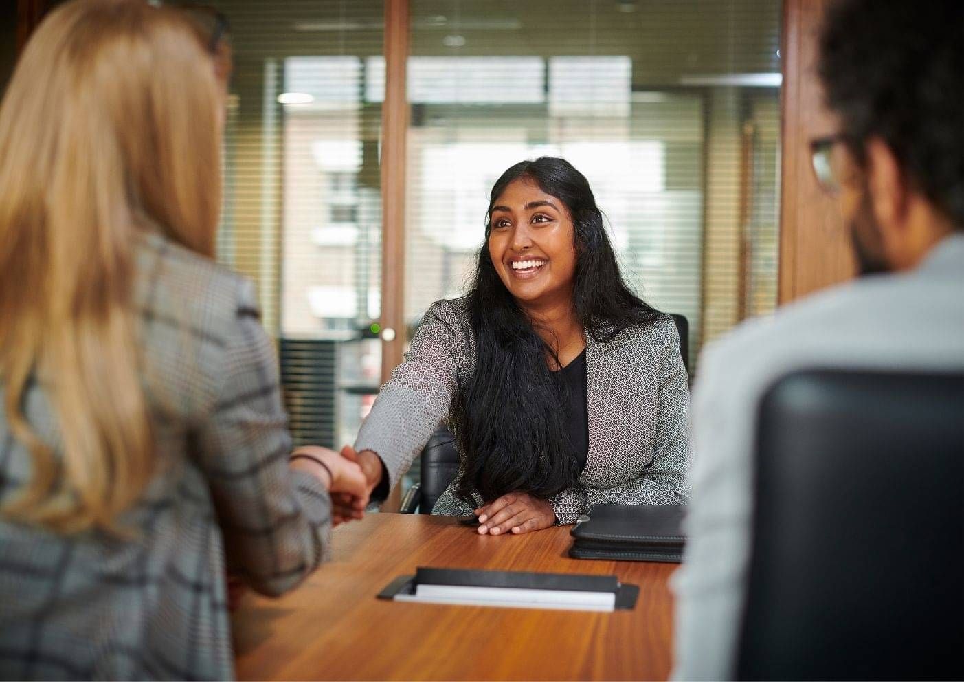 Job candidate and employer shaking hands across a desk after agreeing a new role