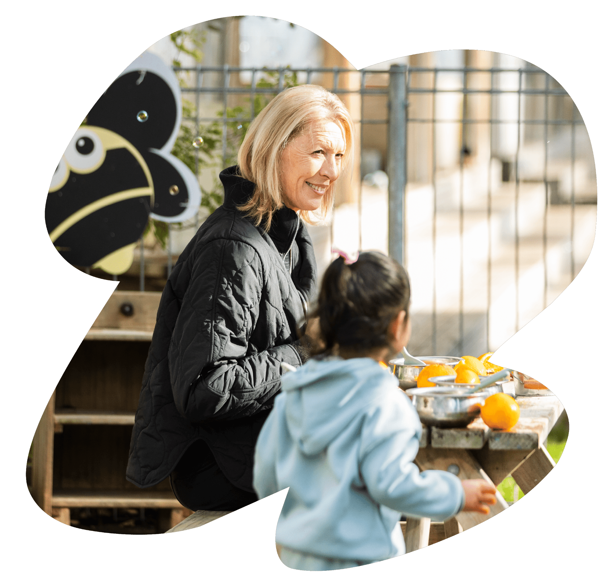 A Sunshine Childcare teacher talking with a child during outdoor play.