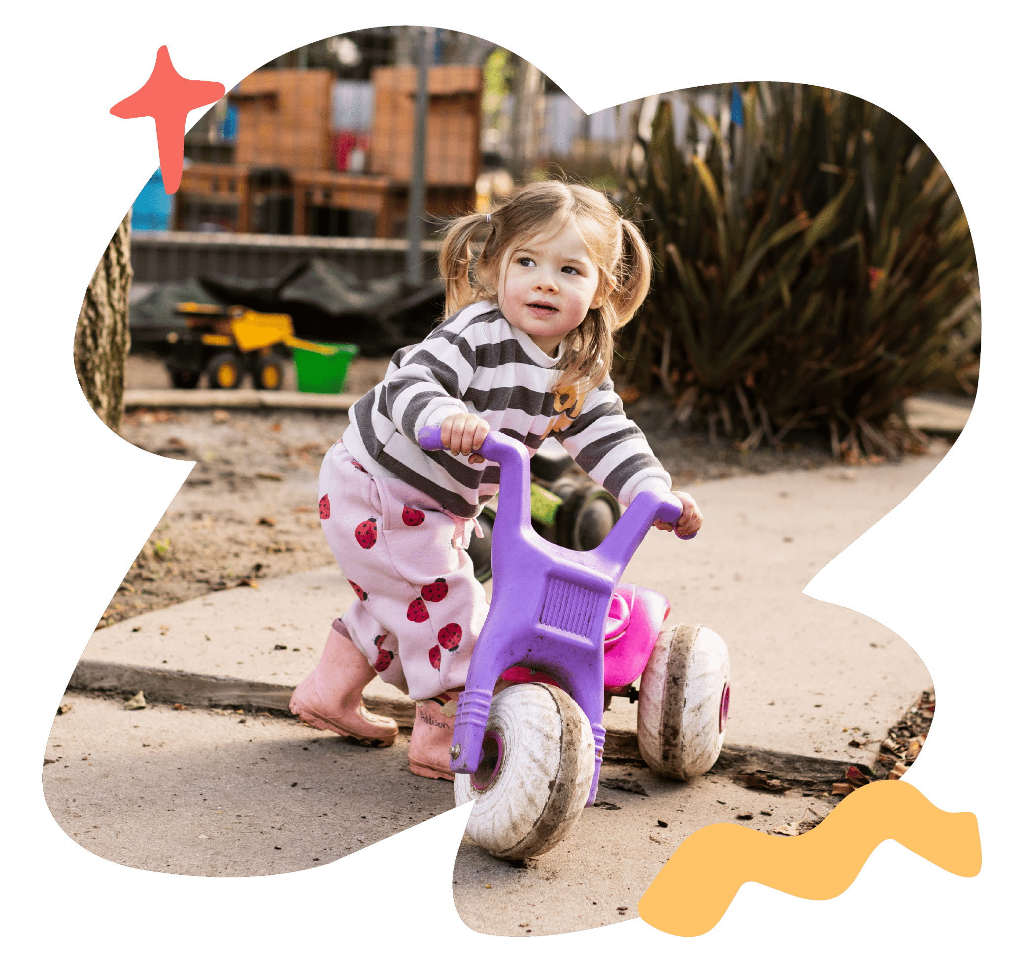 A toddler riding a purple tricycle in the Sunshine Childcare playground.